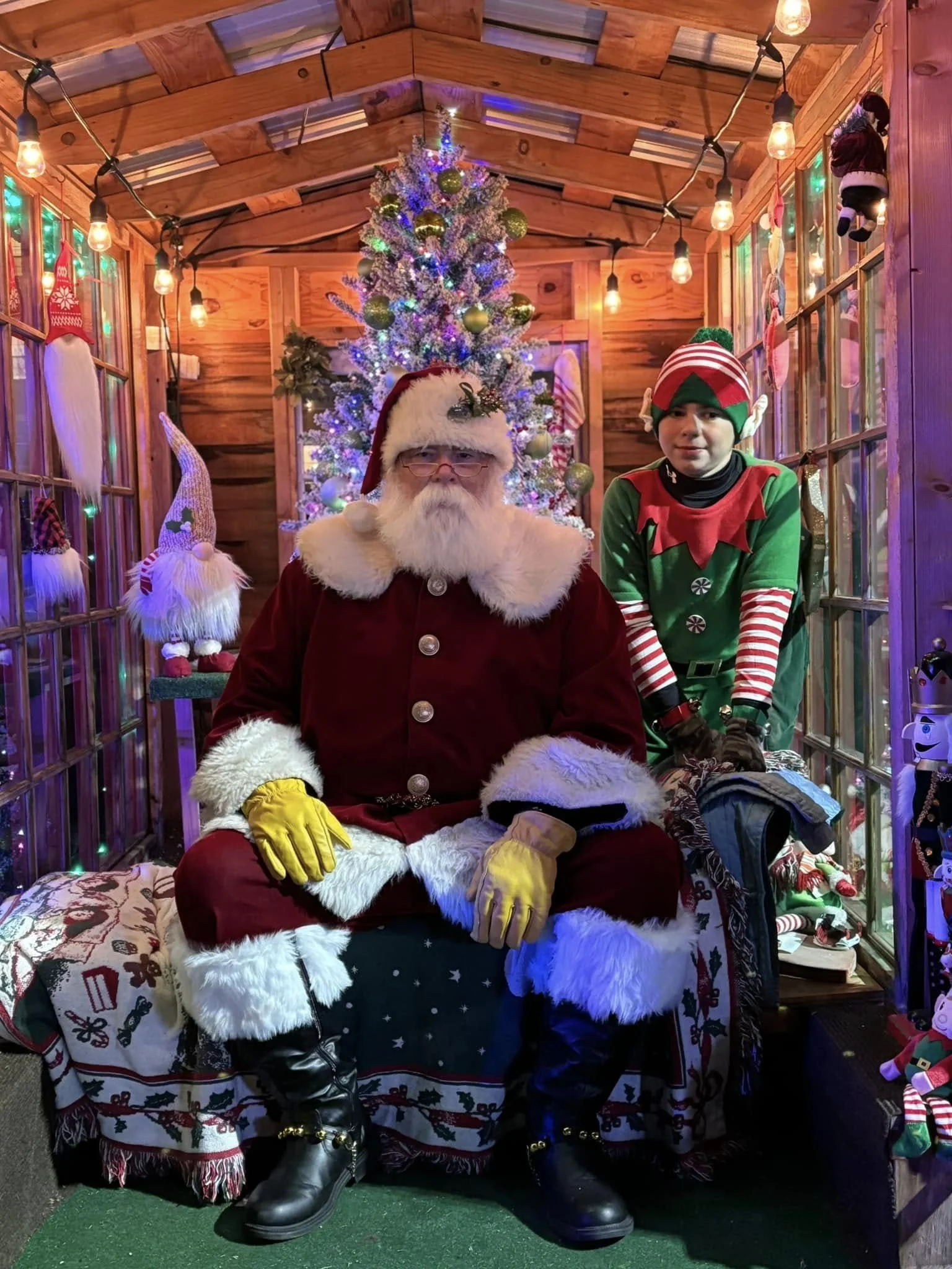 Santa Claus with an elf ready for families and free Santa photos during lamplight stroll.