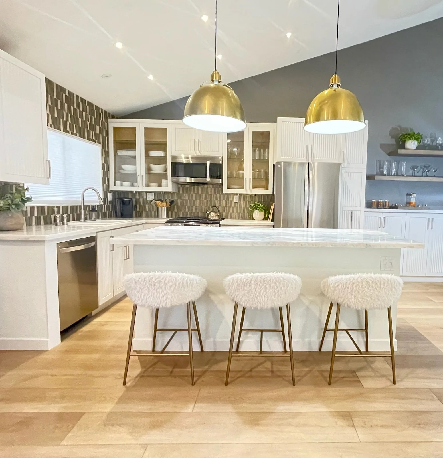 A contemporary kitchen staged with white fluffy chairs, white cabinets, gold pendants in Palm Springs, CA
