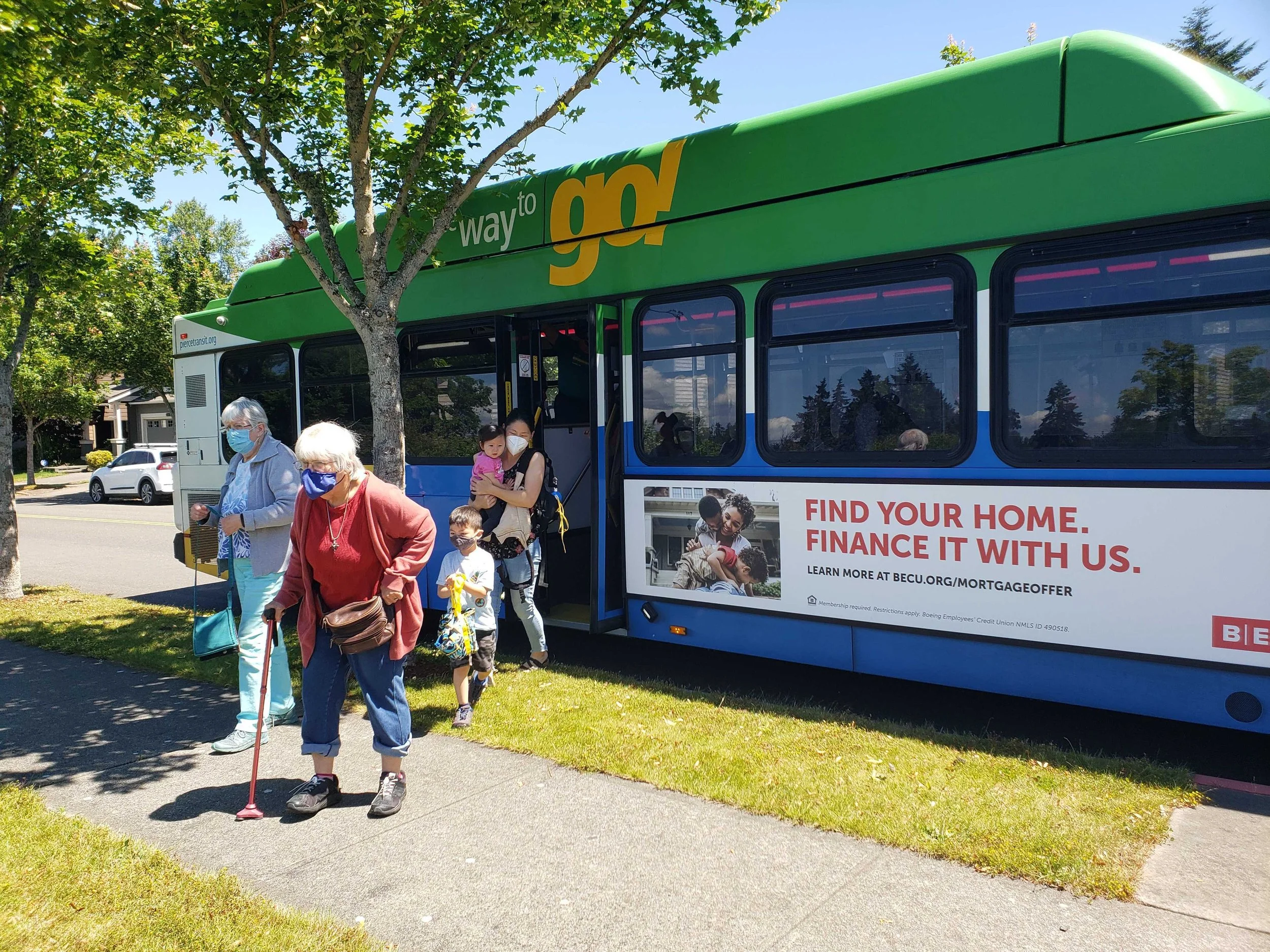 People disembark from a Pierce Transit bus, including an elderly woman with a mask and a cane.