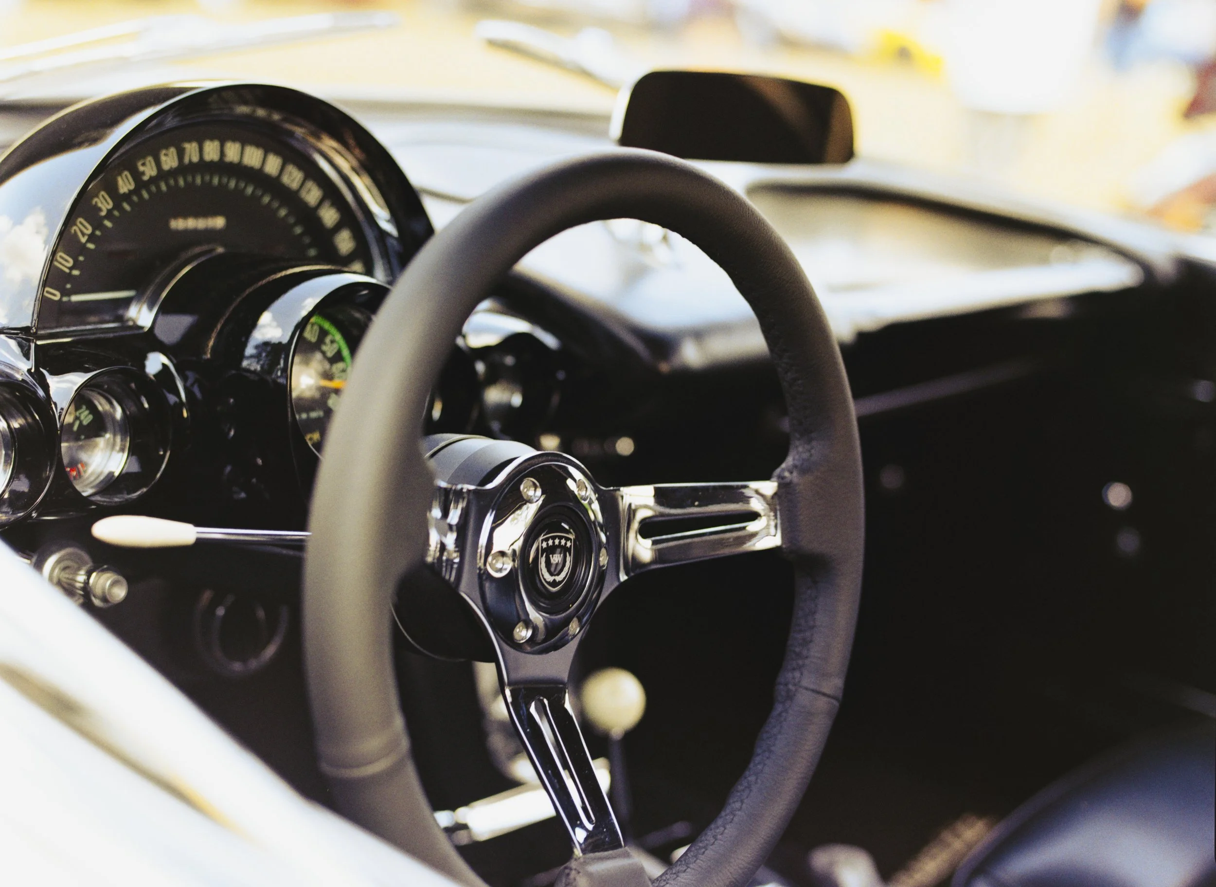 Close-up of a vintage car's interior, showing the steering wheel and dashboard with speedometer and gauges.