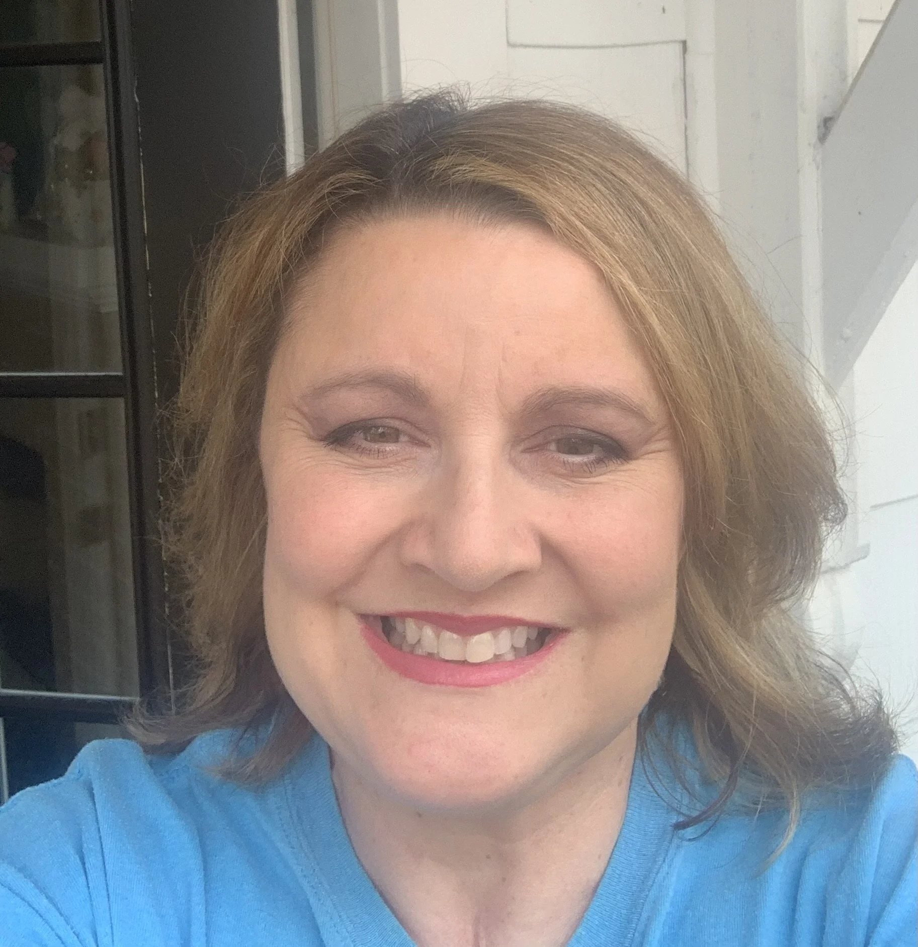 Smiling woman with light brown hair, wearing a blue top, in front of a gray and white indoor background.