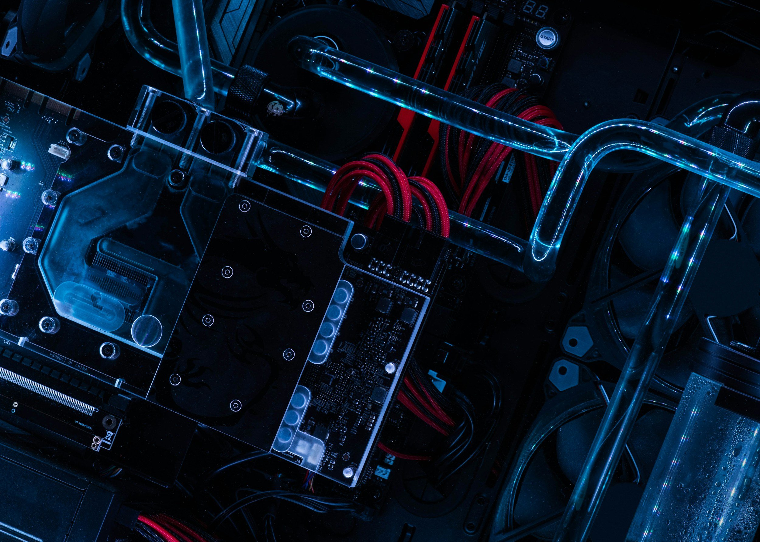 Close-up of the interior of a computer with visible motherboard, liquid cooling tubes, and cables, illuminated with blue lighting.