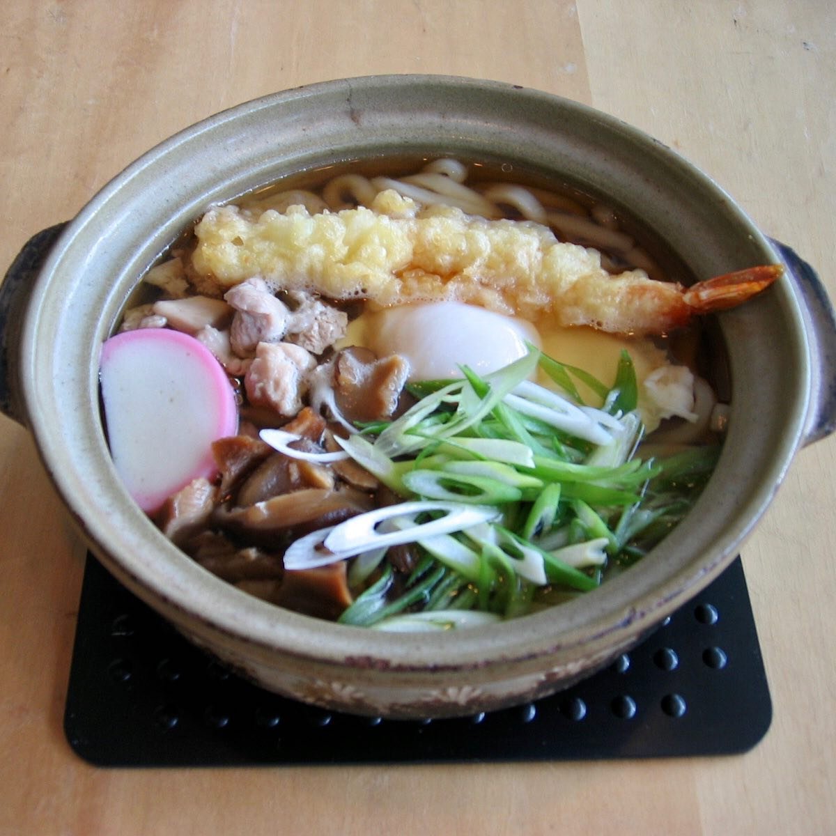 A bowl of Japanese noodle soup with tempura shrimp, sliced fish cake, green onions, mushrooms, and soft-boiled egg.