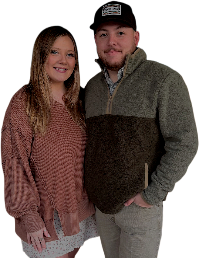 A young woman with long brown hair wearing a pinkish-brown sweater and a light-colored skirt, standing next to a young man with a beard wearing a cap and a two-tone fleece jacket, smiling together against a black background.