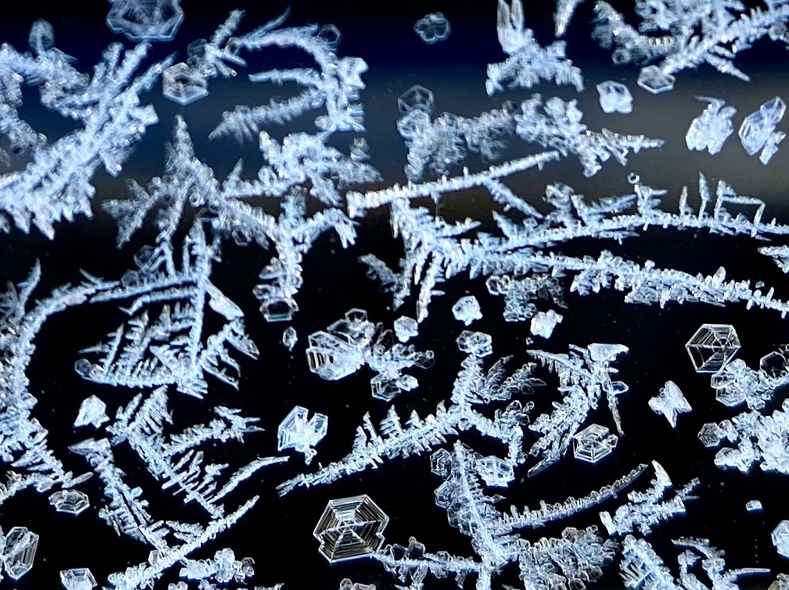 Close-up of intricate, sparkling ice crystal snowflakes on a dark surface.