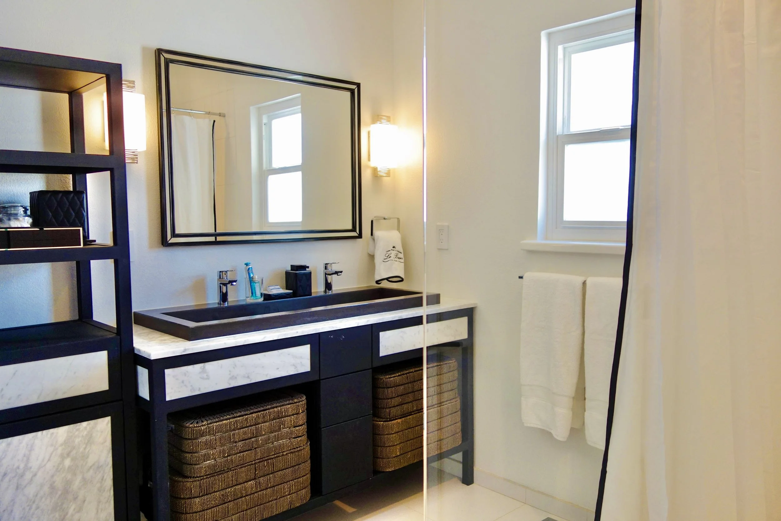 Bathroom with a black vanity, white marble countertop, rectangular sink, large mirror, and a window with natural light.