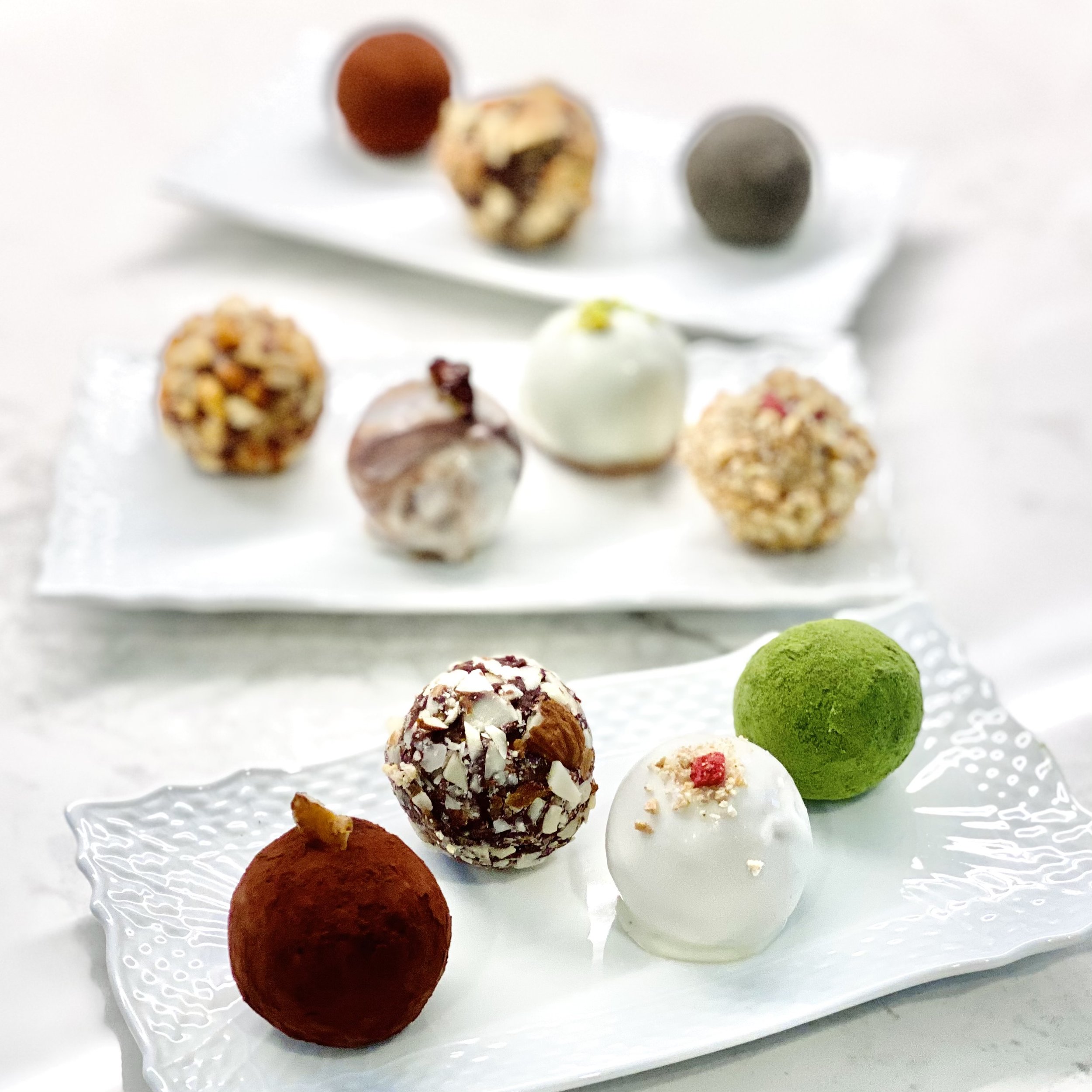Assorted colorful truffles and chocolate candies on a white glass tray.
