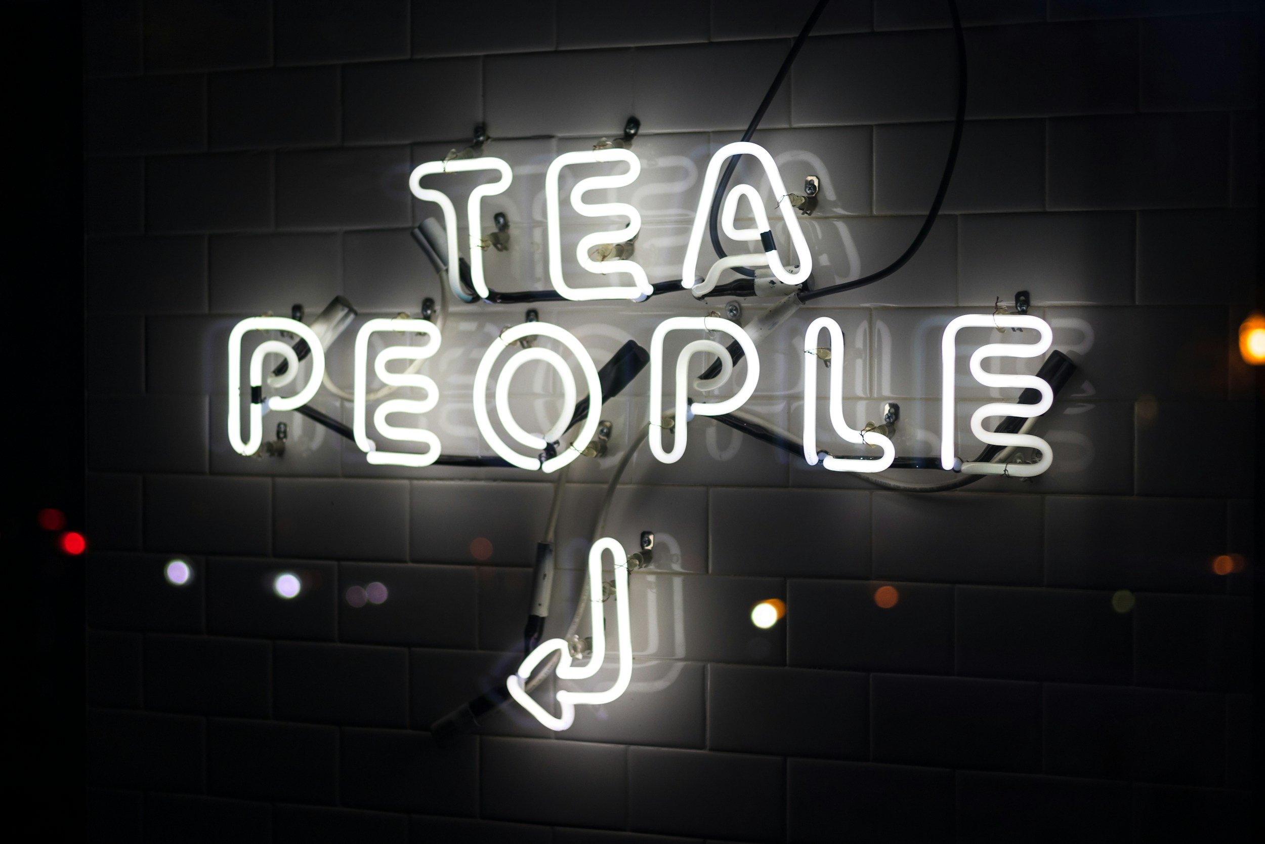 A neon sign with the message 'TEA & POPS' on a dark tiled wall.