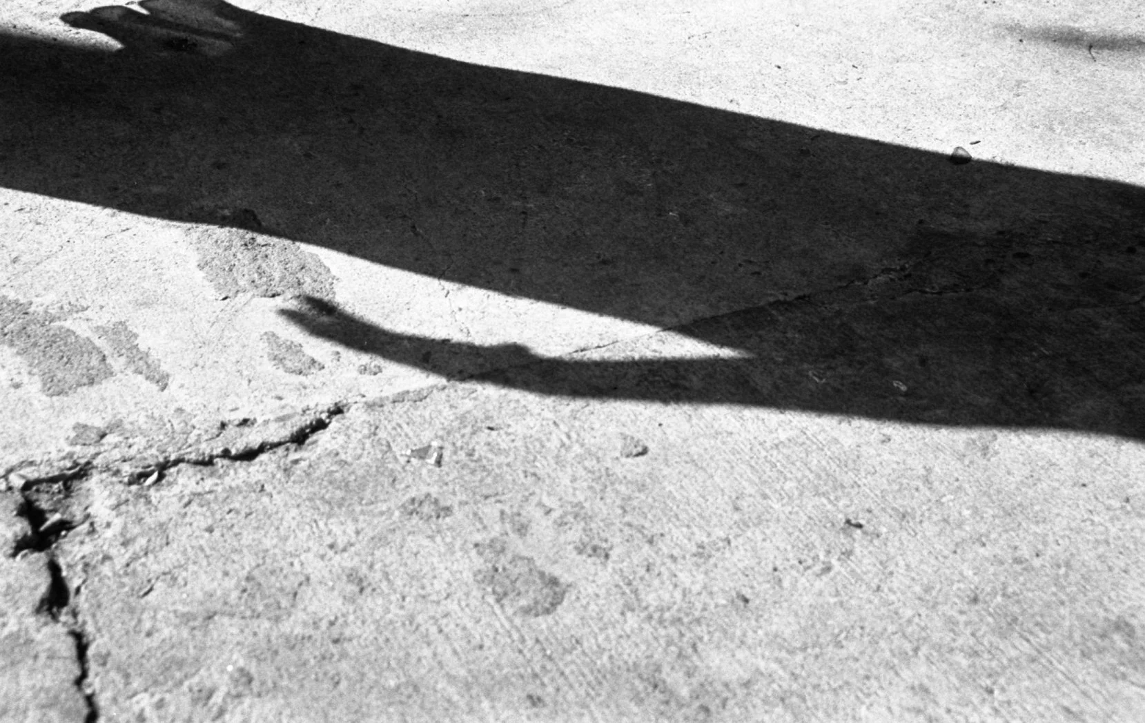 Shadow of a person on a cracked concrete sidewalk and a wall, in black and white.