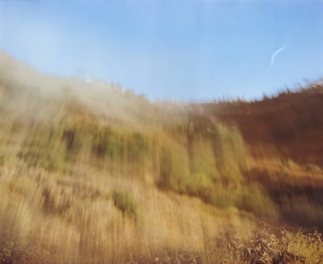 Blurred image of a mountain landscape with a blue sky and some trees.