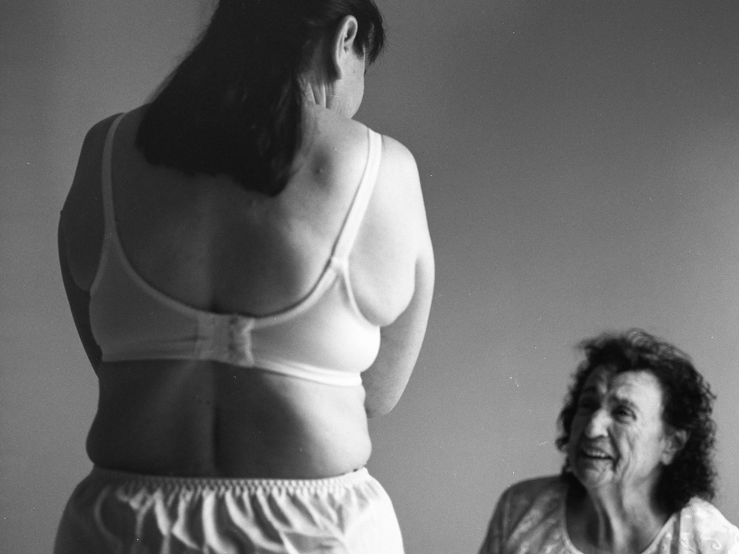 Black and white photo of a woman in a tank top, turned to the side, with a smiling older woman in the background.