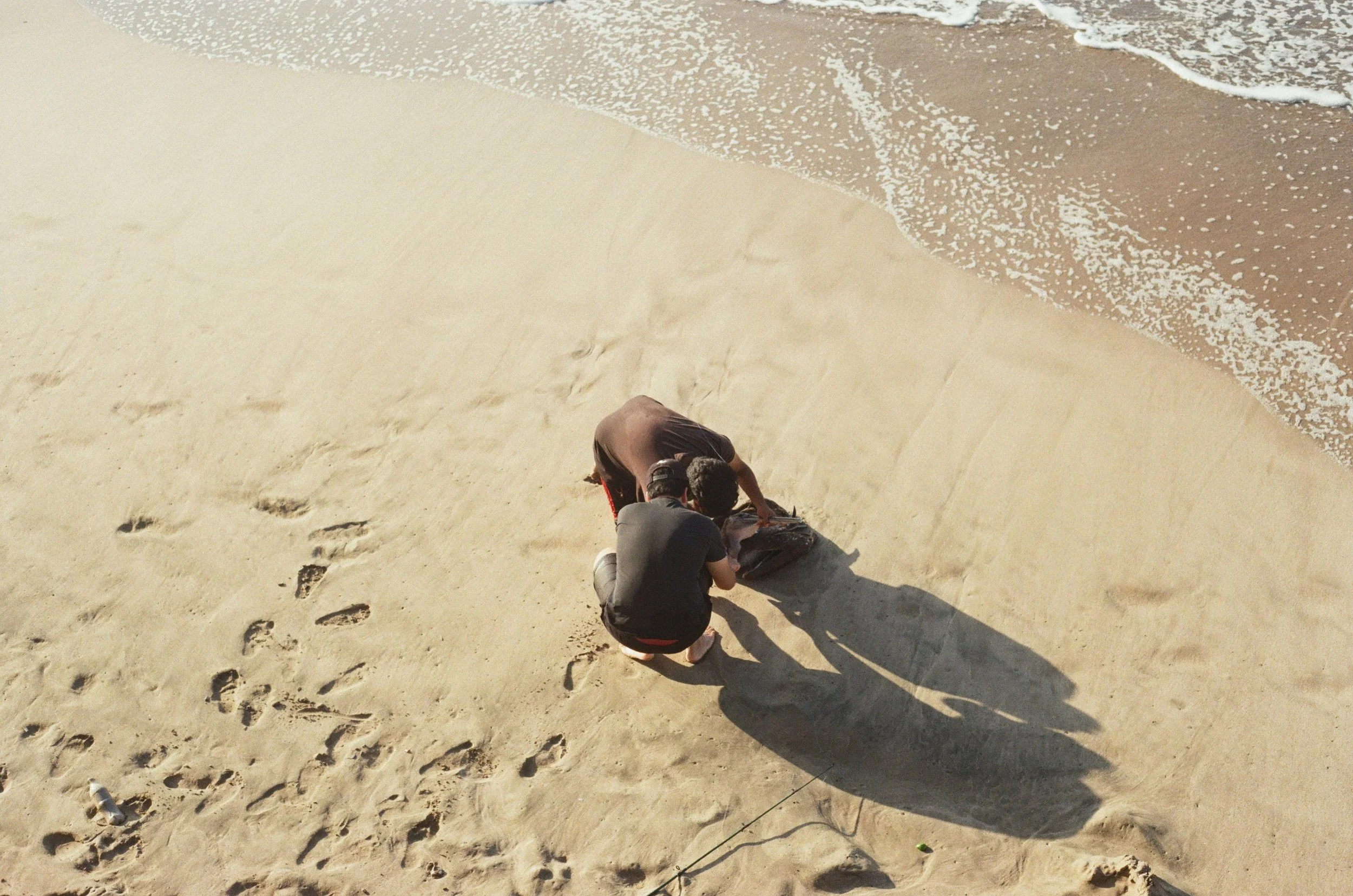 Two children building a sandcastle on a sandy beach near the shoreline with footprints and seaweed.