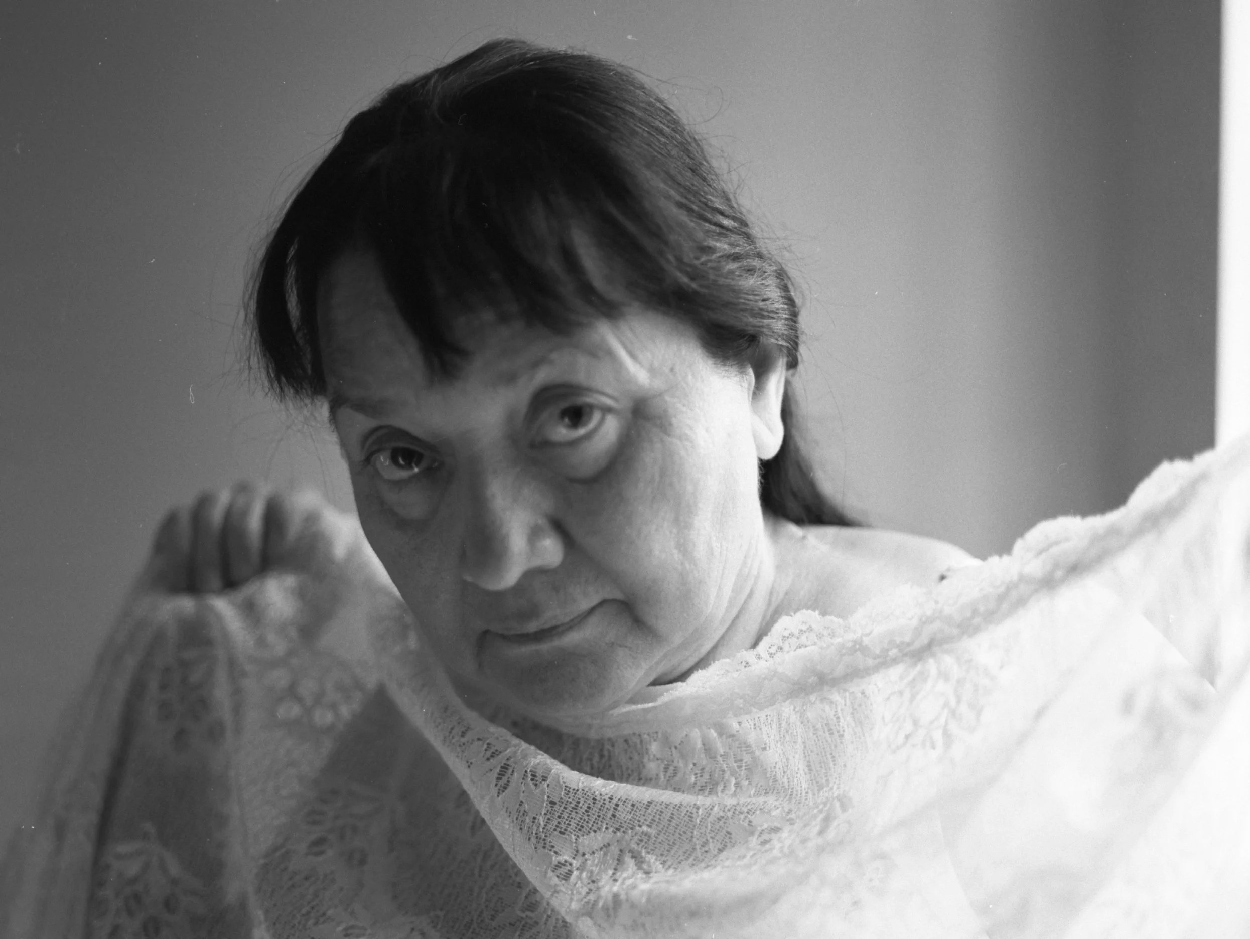 Close-up of a person's face with short dark hair, wearing a lace garment, looking downward.