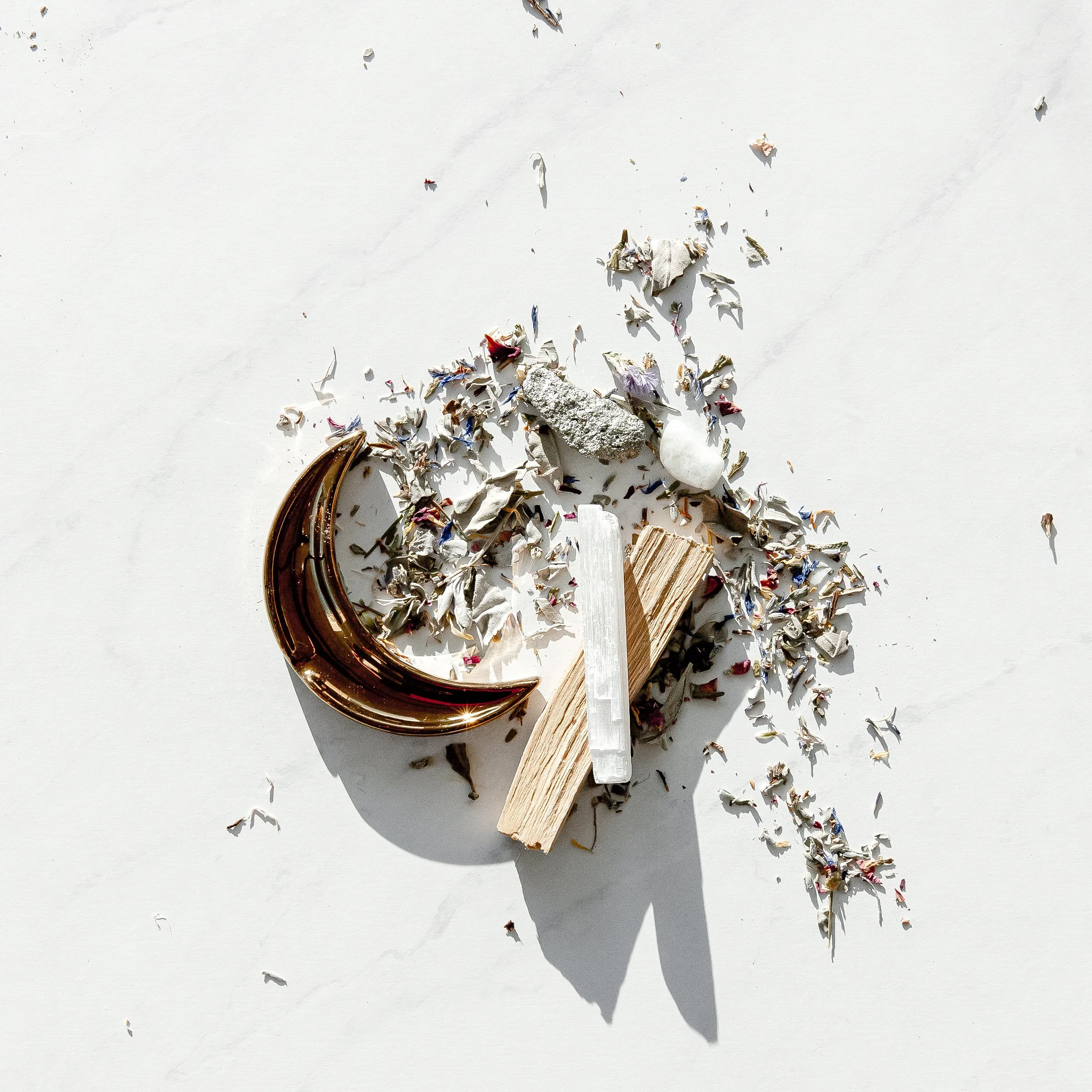 Scattered crumpled paper pieces, some with colorful printing, on a white surface. A small white object, possibly a stone, and a piece of wood are among the debris. The image is partially in shadow from a curved metallic object on the left side.