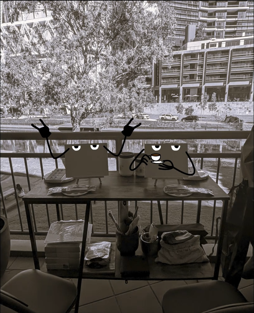 Black and white photo of a balcony with two animated character boxes with faces, arms, and expressions. One is pointing up with both hands; the other is holding a cup. There are plates, napkins, and utensils on a table, with a view of trees, a body of water, parked cars, and modern buildings in the background.