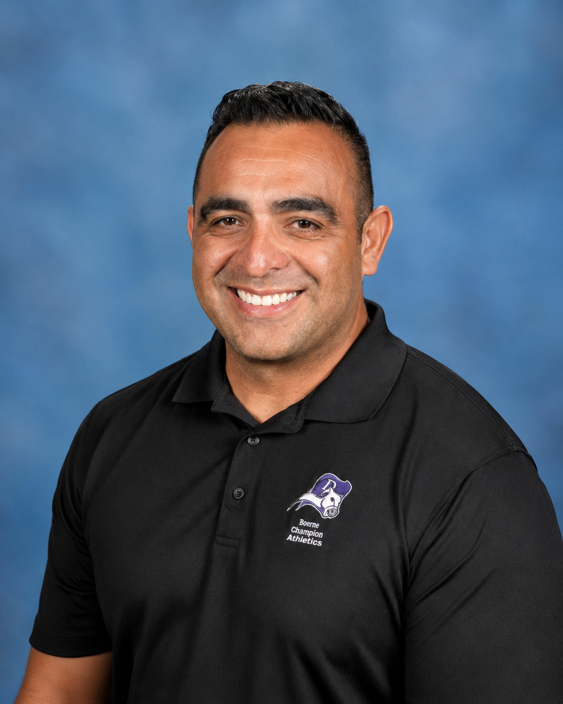 Smiling man in black polo shirt with 'Boerne Champion Athletics' logo, posing against a blue background.