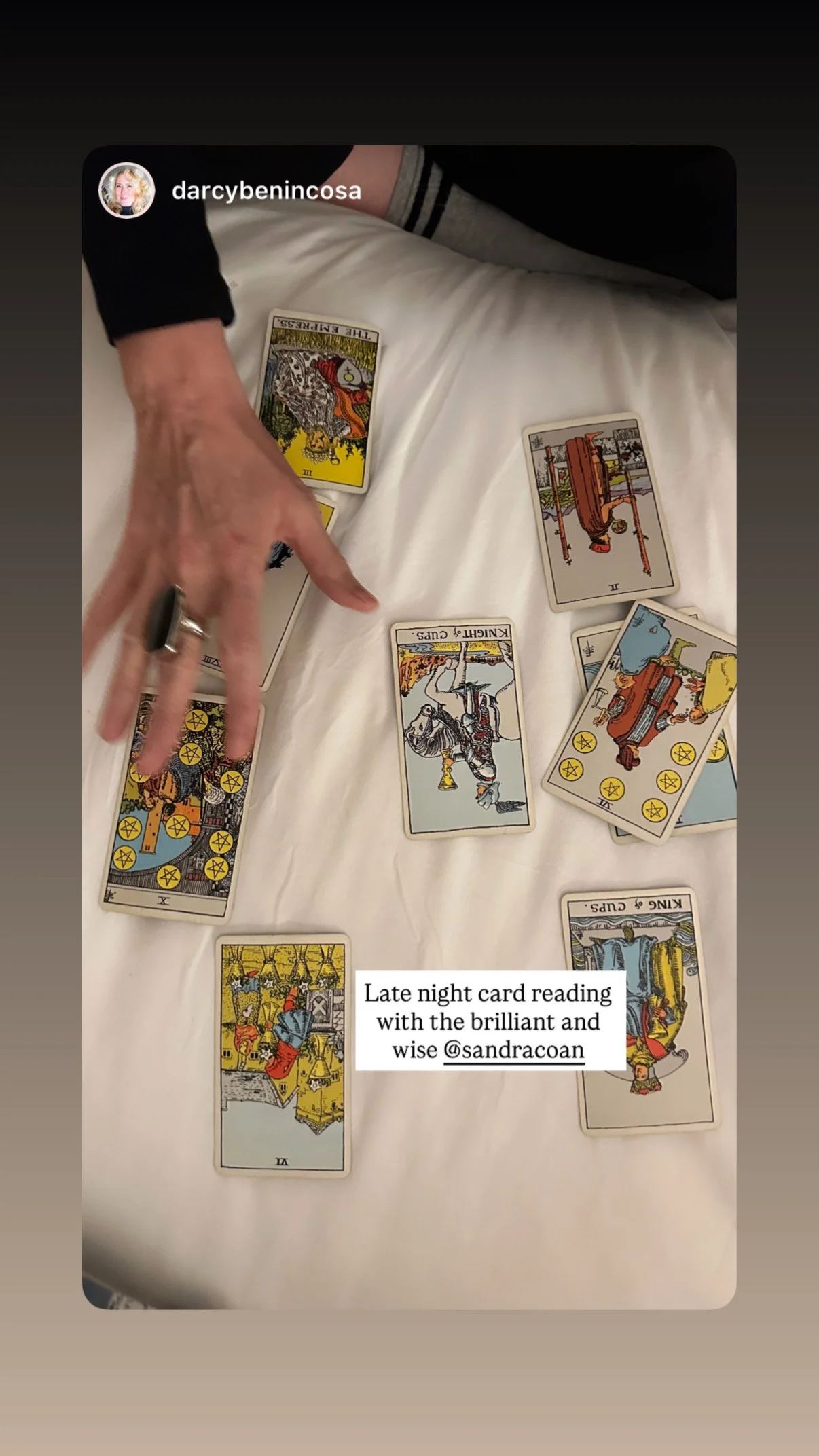 People reading tarot cards on a bed, with some cards spread out on the bed and one person pointing to a card.