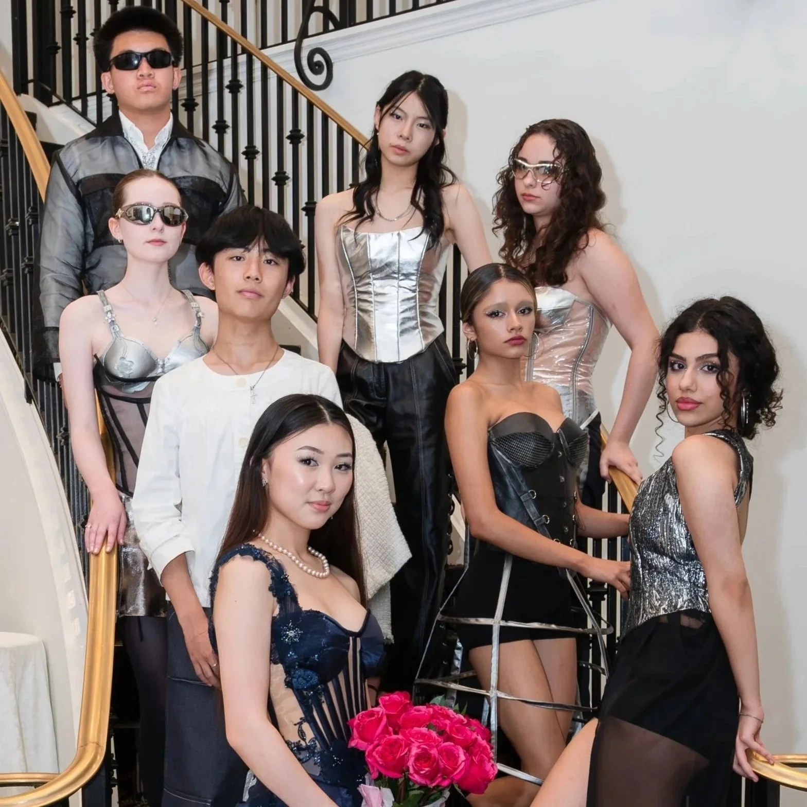 Group of models posing on a staircase, dressed in fashionable, futuristic attire with some wearing sunglasses.