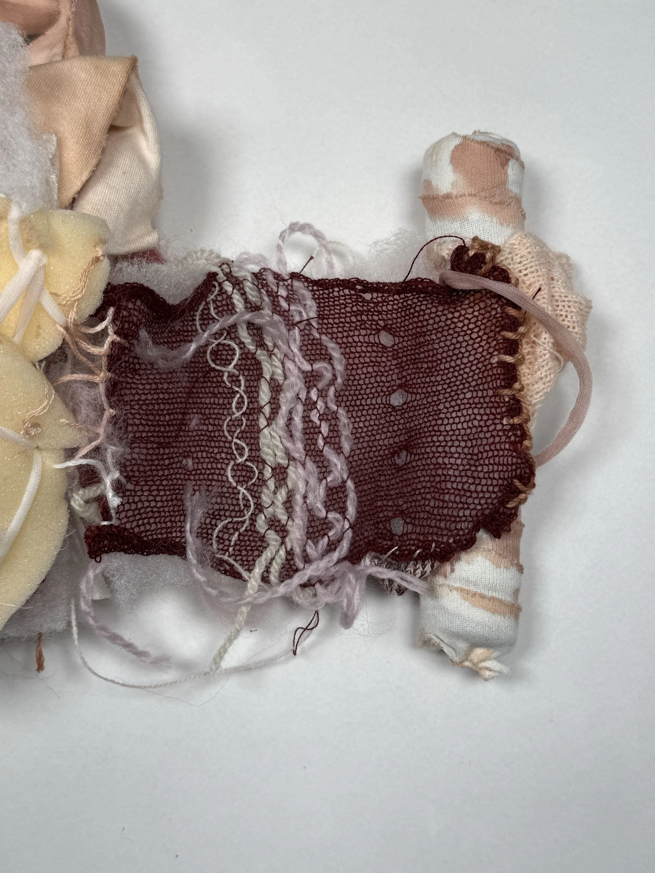 Close-up of a fabric doll made from various textiles, including lace, netting, and sock material, with some frayed edges and loose threads.