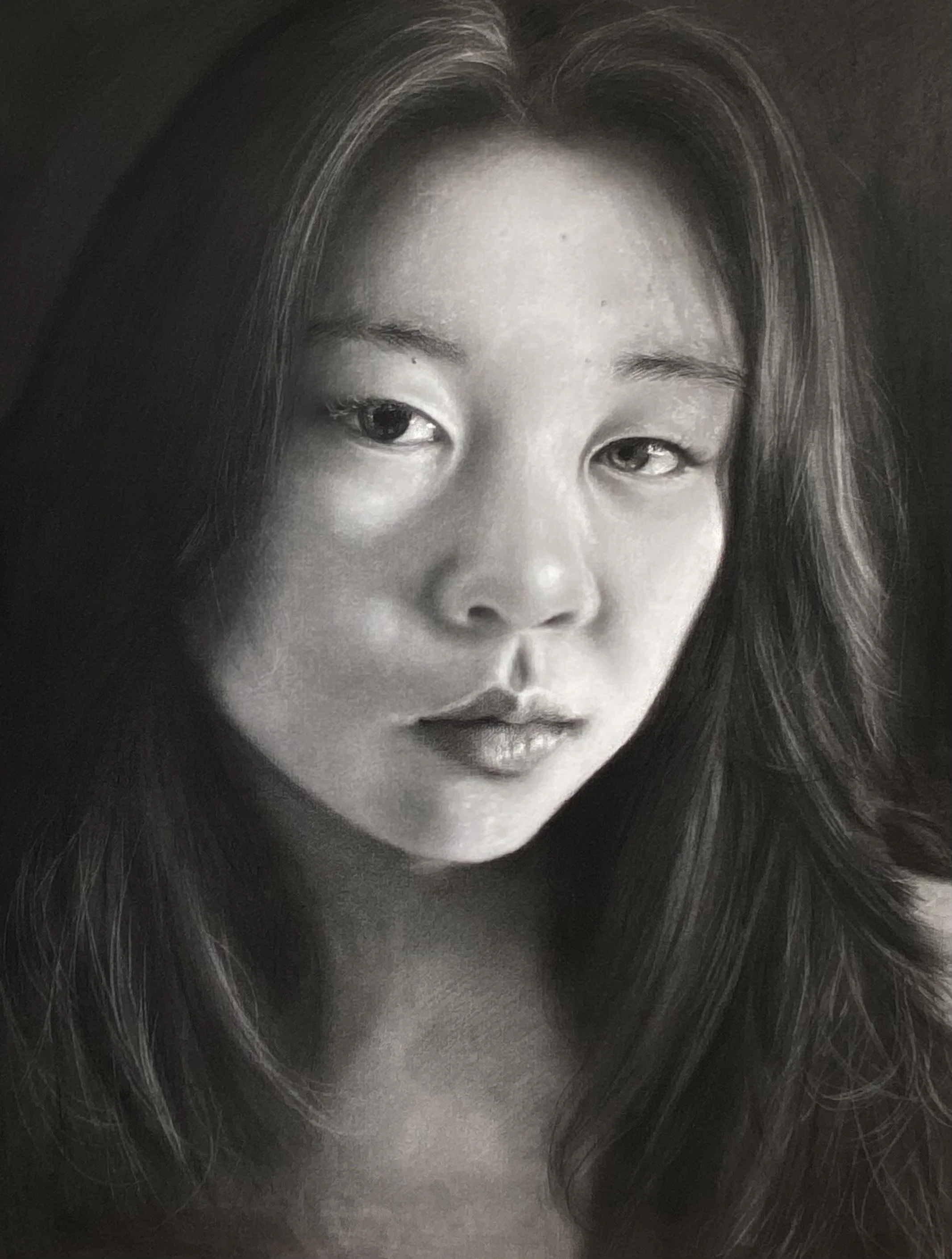Close-up black and white self portrait looking slightly downward, with a serious expression.