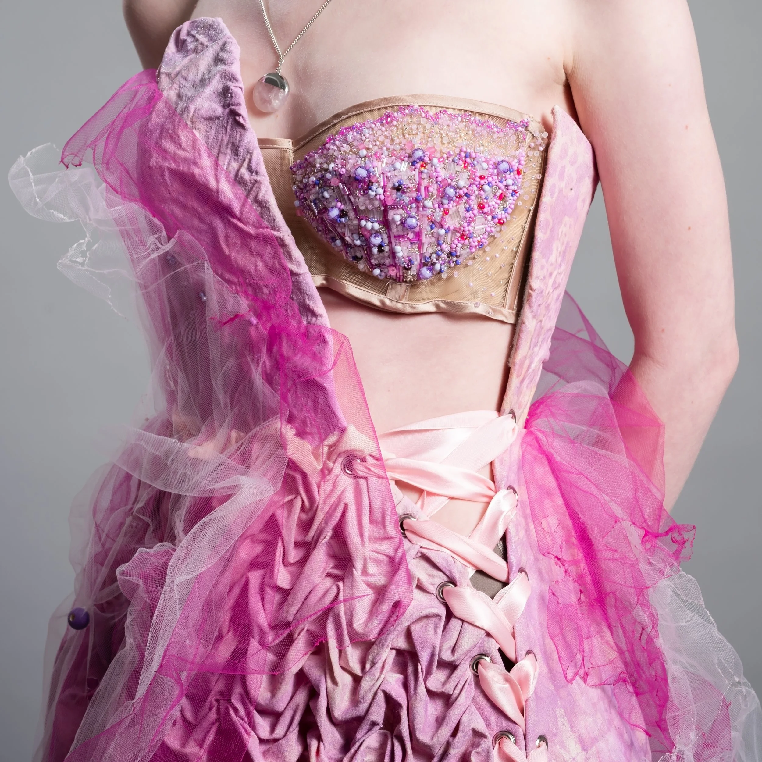 Close-up of a woman wearing a pink, bejeweled corset top and pink tulle fabric draped over her shoulder.
