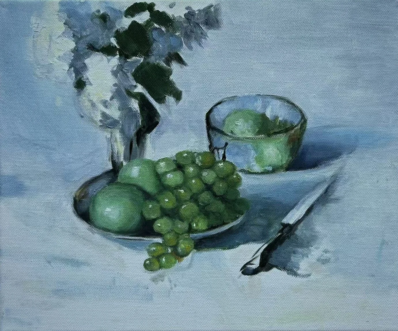 Still life painting of green grapes, limes, a glass bowl with limes, a knife, and a vase with flowers on a table with a blue background.