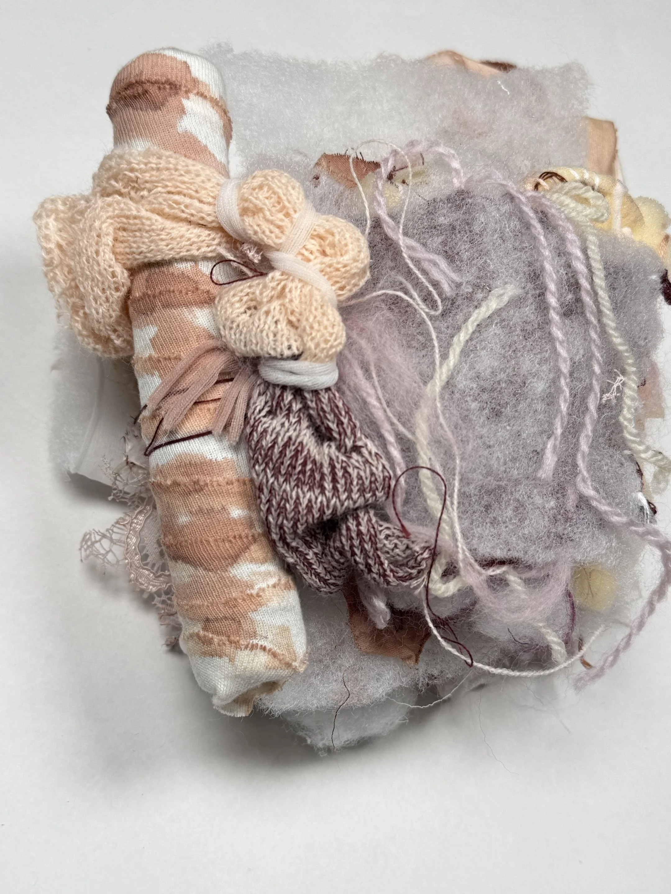 Close-up of various small fabric and yarn materials, including knitted socks and wool, arranged on white paper.