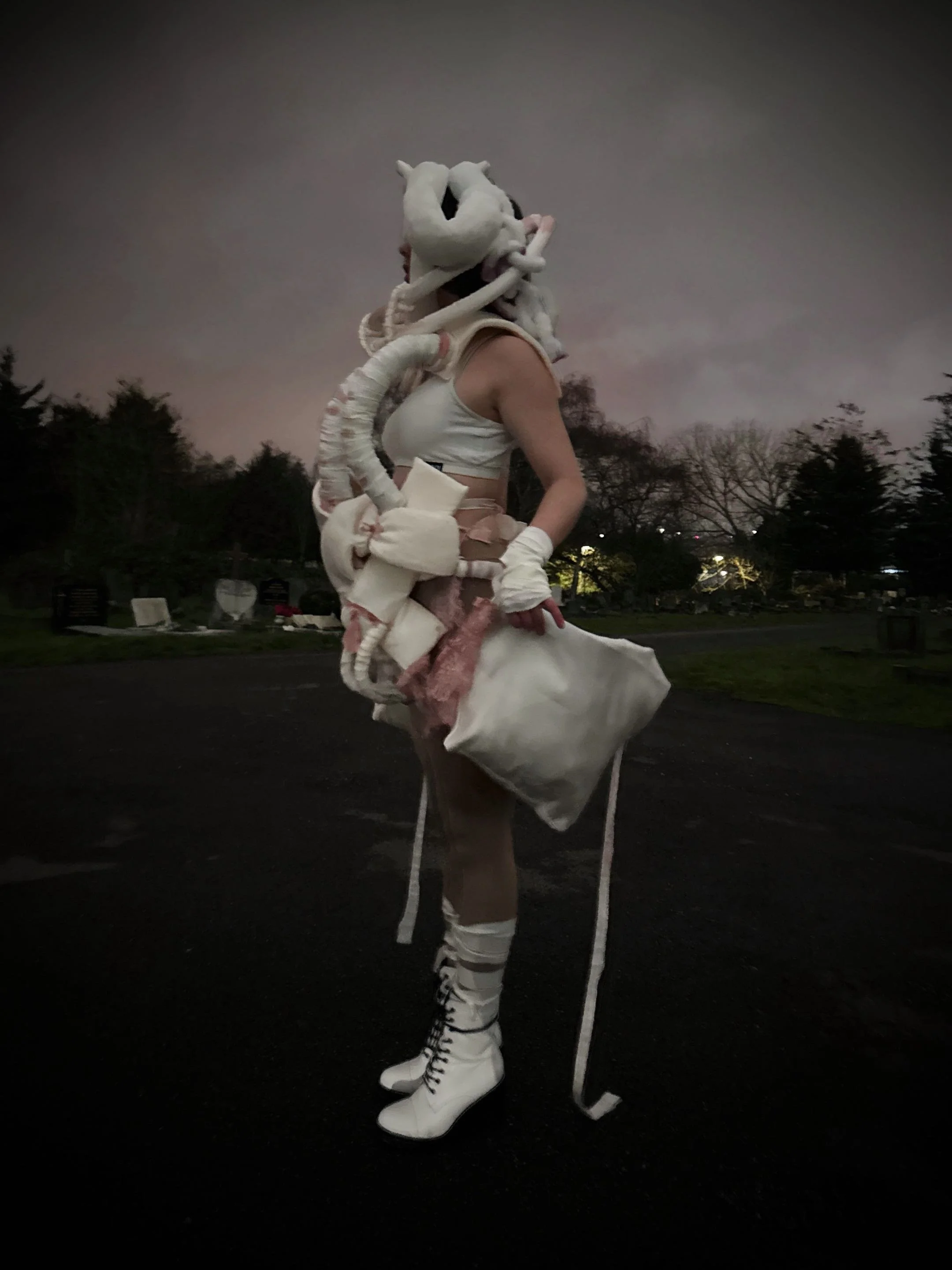 A model standing outside at dusk wearing a white headpiece and outfit.