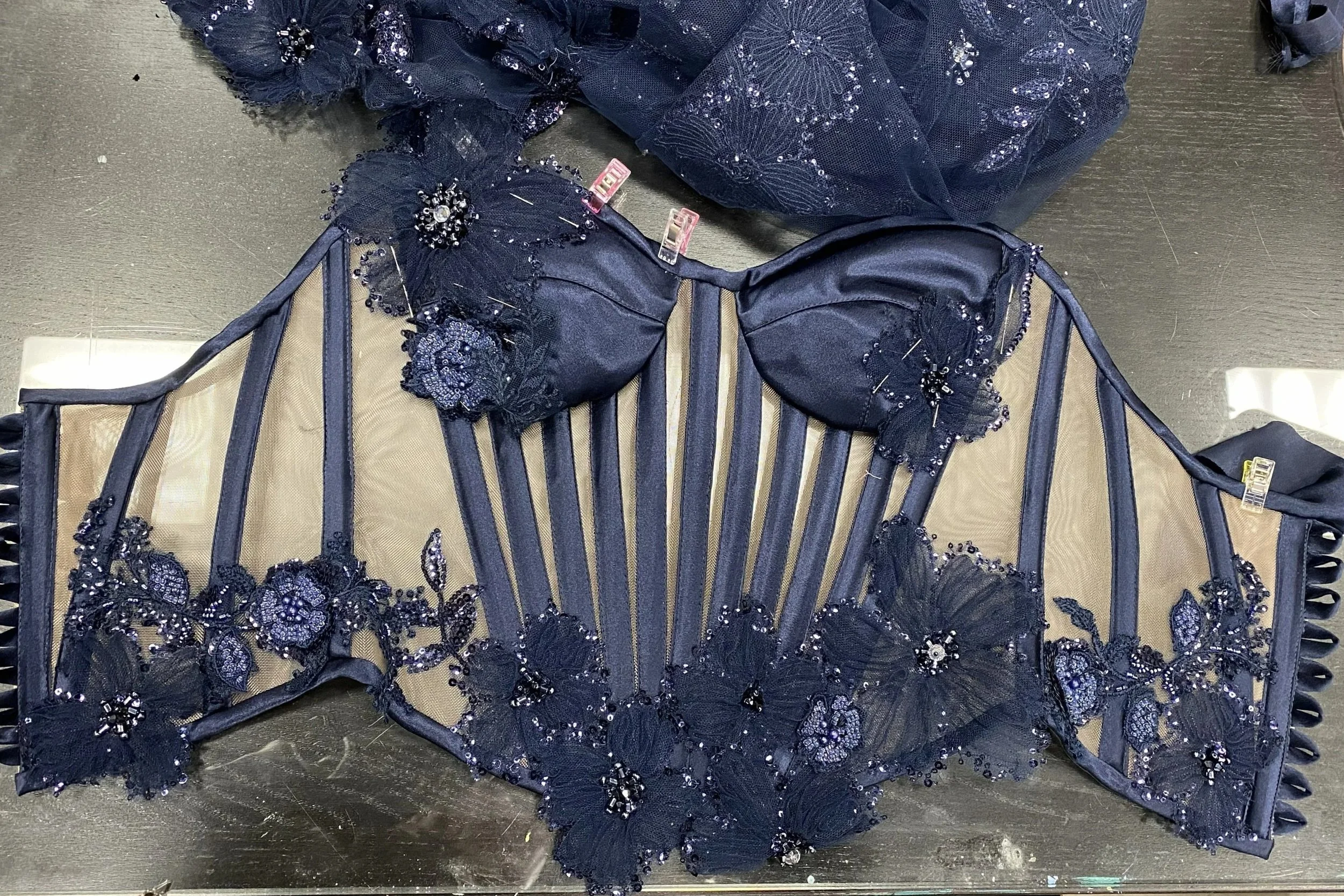A dark blue lace dress with intricate floral embroidery and sequins, resting on a black surface.