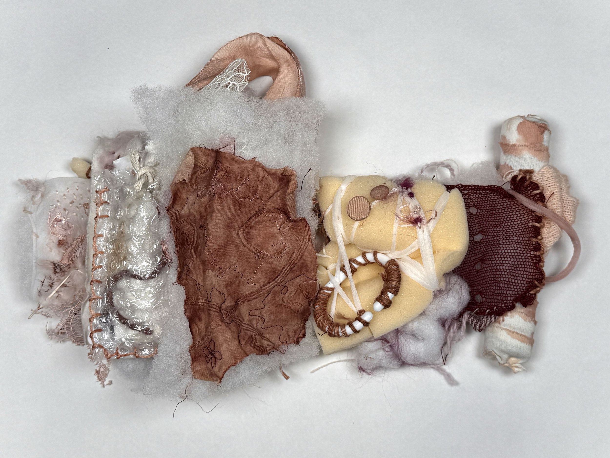 Various pieces of fabric and textile materials in shades of beige, brown, and cream are arranged on a white background, including lace, ribbons, and textured fabrics.