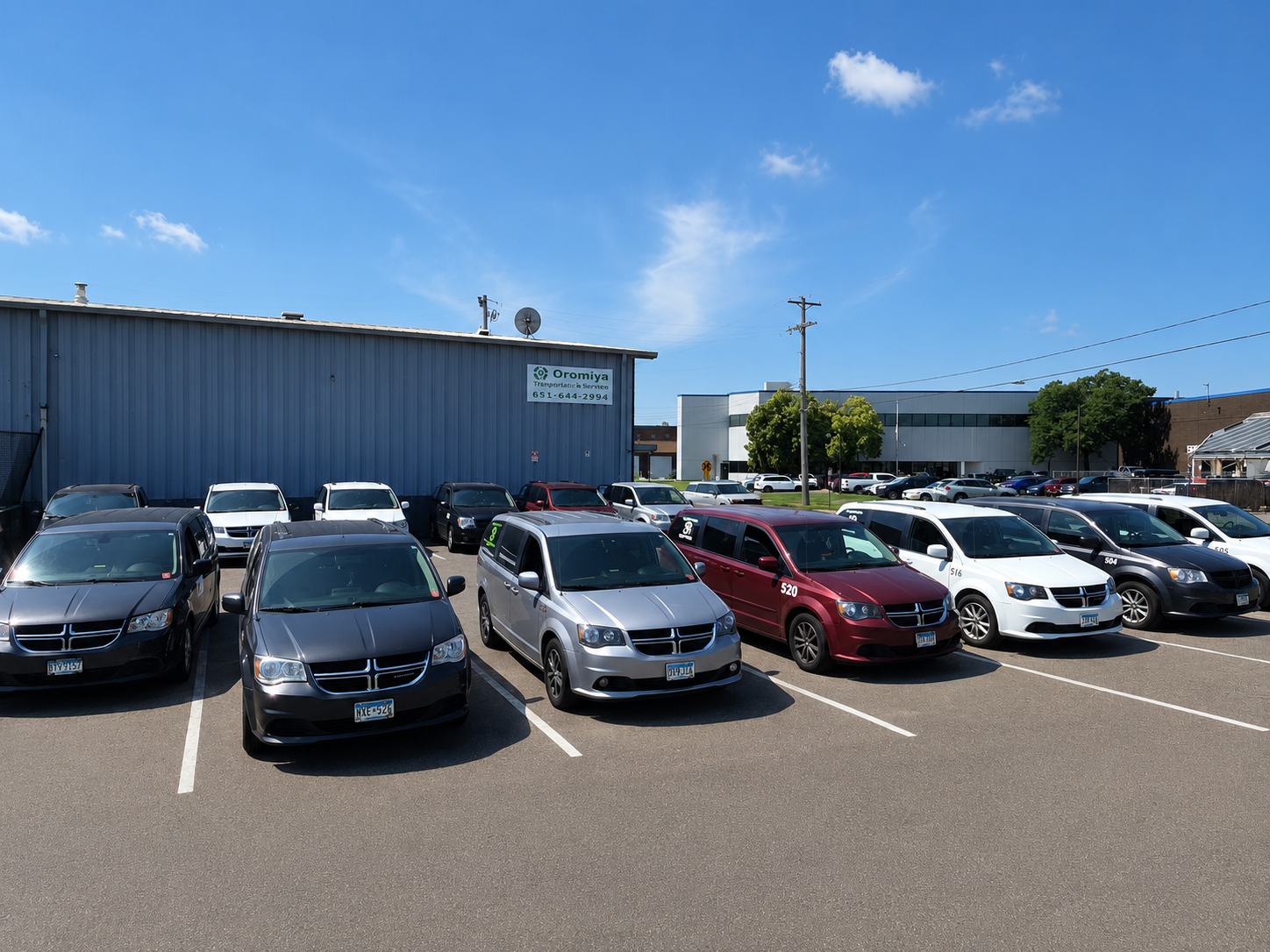 Parking lot filled with various cars in front of a blue industrial building with a sign that reads 'Oromiya Transport & Service' under a blue sky with a few clouds.