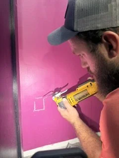 Man using a yellow cordless drill on a pink wall