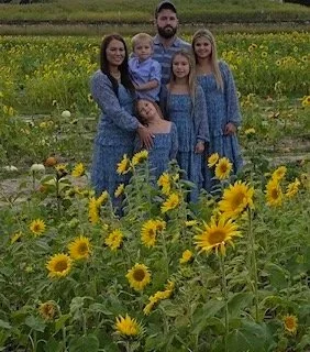 A family of five standing in a sunflower field.