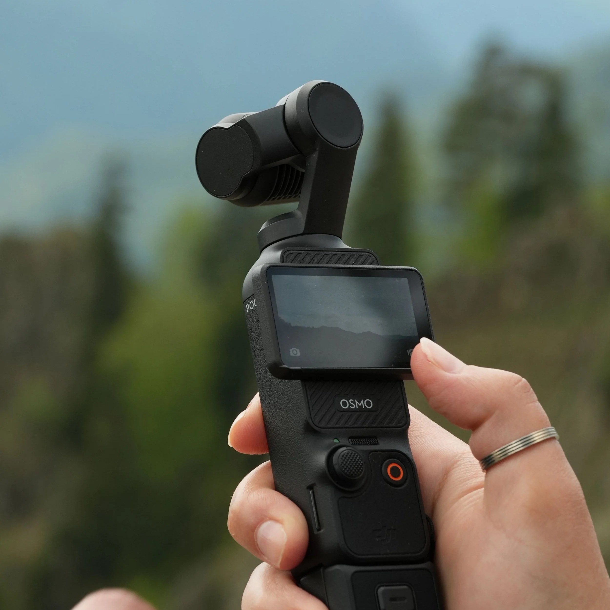 Person holding a DJI Osmo Pocket gimbal camera outdoors, with a blurred natural background.
