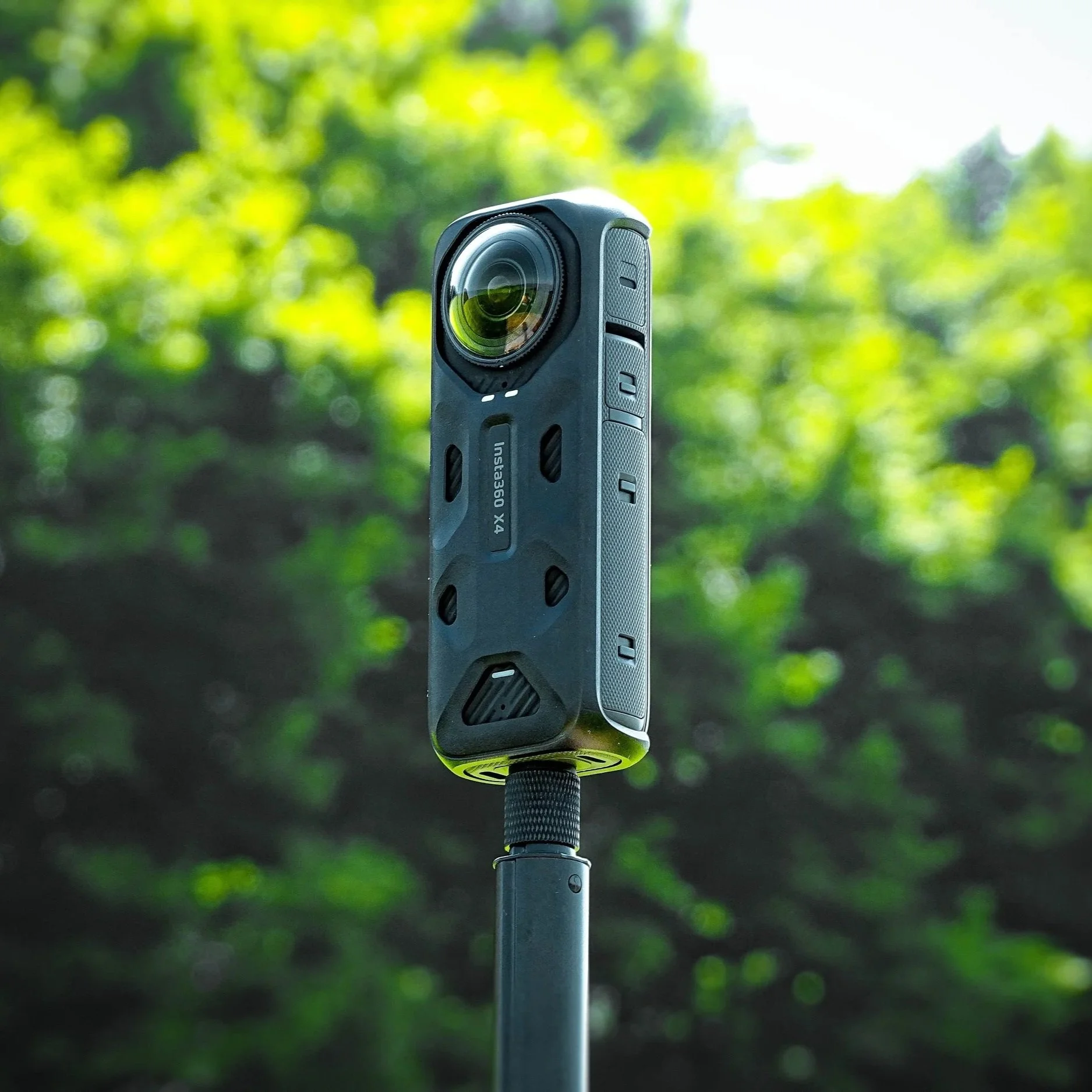 A handheld camera mounted on a pole, set outdoors against a background of blurred green foliage and sunlight.