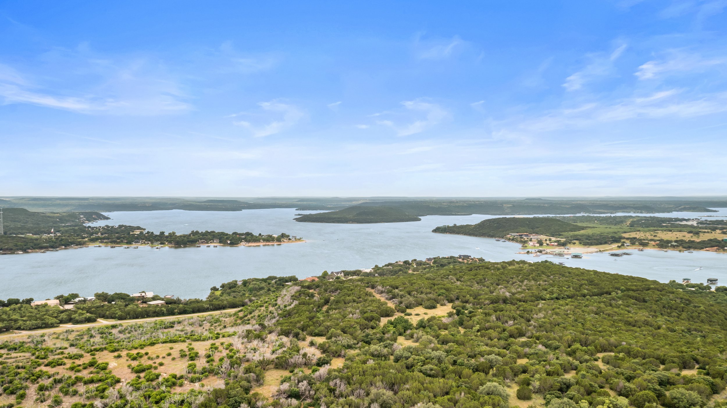 A wide river with green hills on both sides under a blue sky with scattered clouds.
