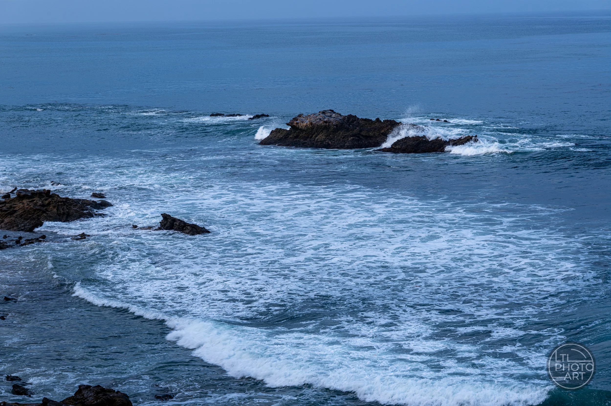 Ocean foam and receding surf surrounding Bird Rock, viewed from an elevated position in Heisler Park, Laguna Beach.