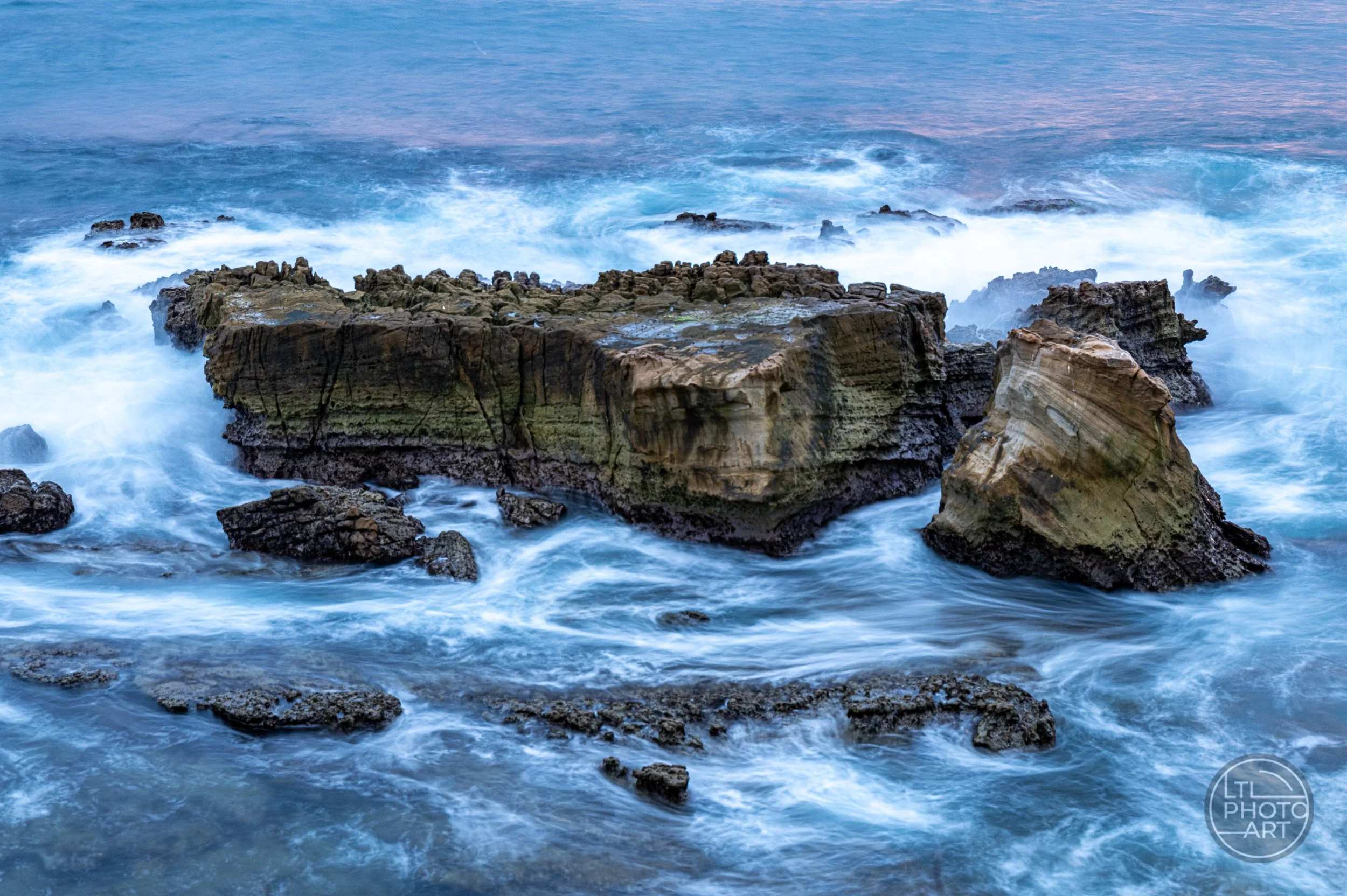 Long-exposure coastal photograph of waves flowing around rock formations at Monument Point in Laguna Beach, California.