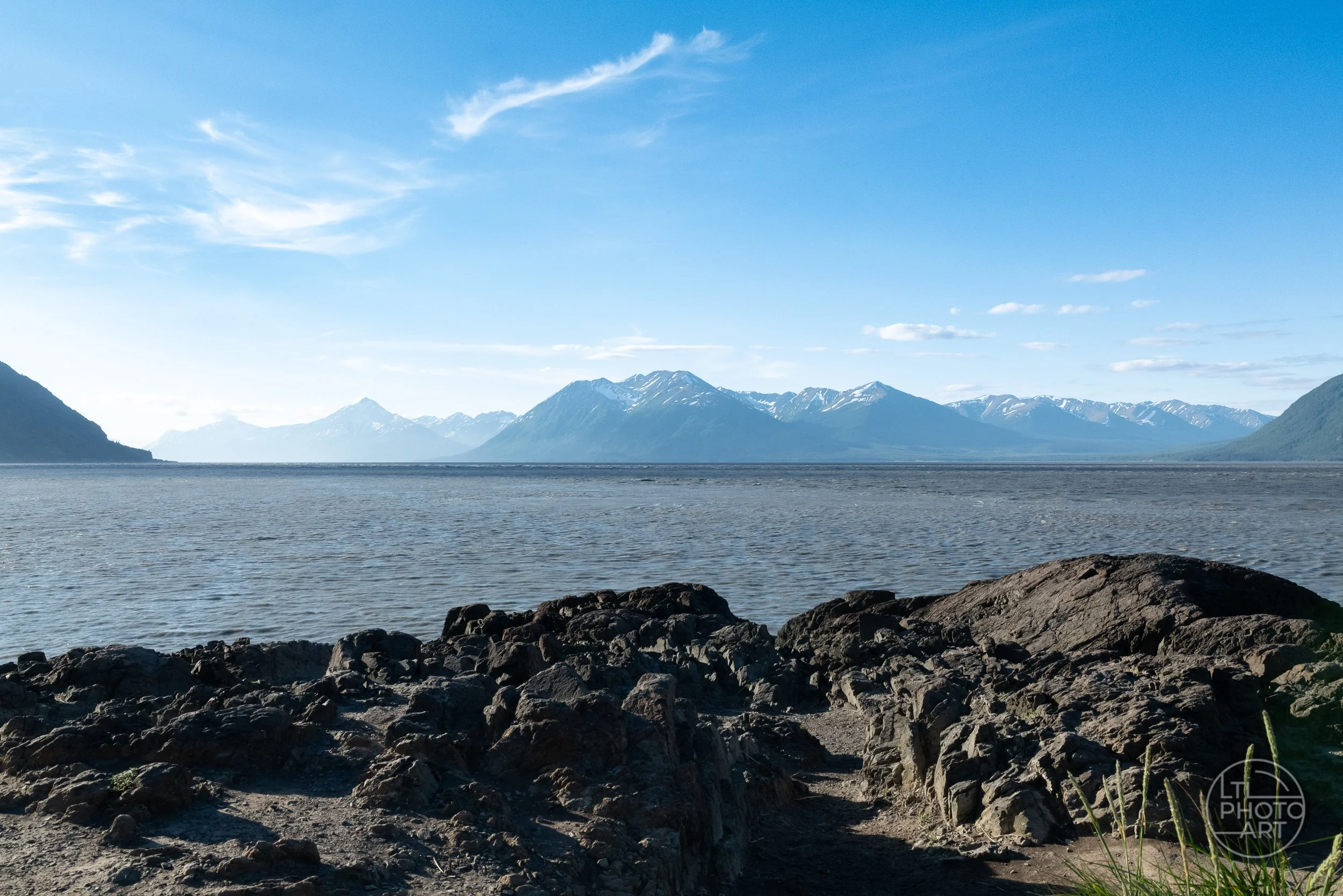 Rocky shoreline overlooking Turnagain Arm and the snow-covered Chugach Mountains along the Seward Highway in Alaska.