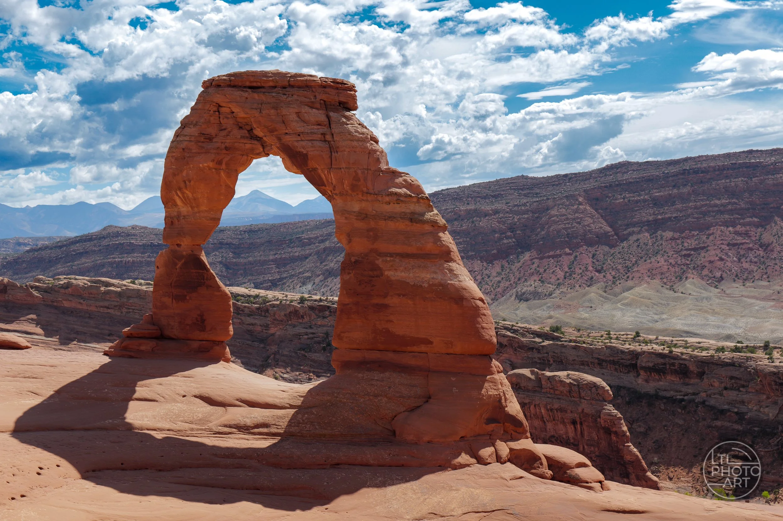 Delicate Arch standing above red rock canyons and distant mountains under a dramatic blue-and-white sky in Arches National Park, Utah.