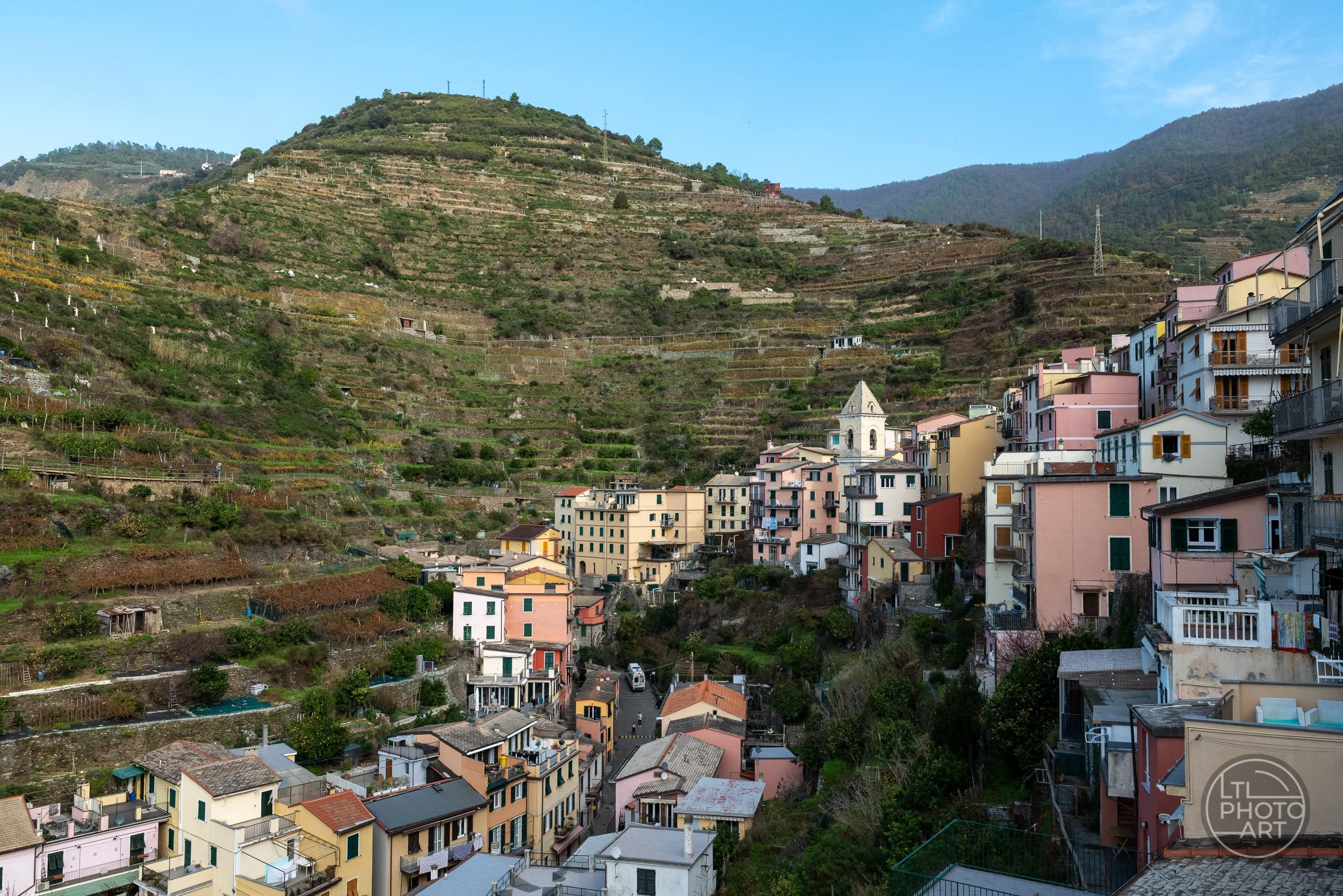 Colorful hillside buildings, a church tower, and terraced vineyards viewed from the Blue Trail above Manarola, Cinque Terre, Italy.