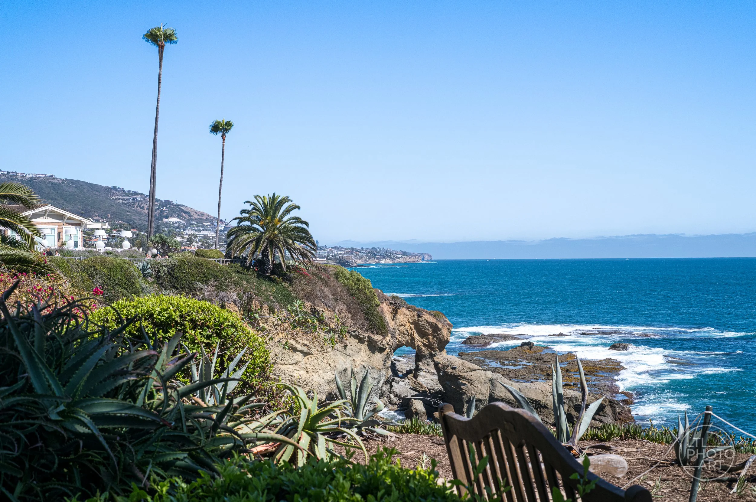 View from Montage Laguna Beach overlooking Treasure Island Beach, its natural rock arch, palm trees, and the Pacific Ocean.