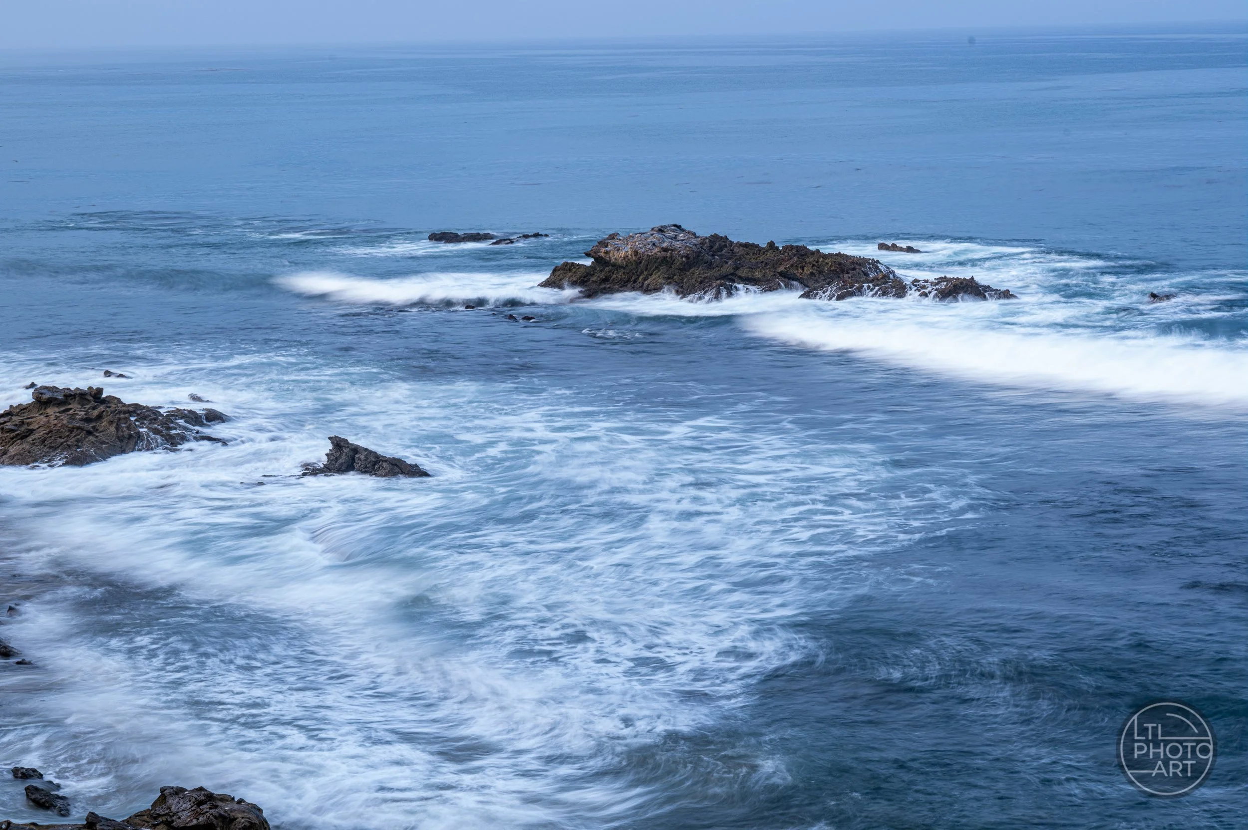 Slow-shutter photograph of whitewater moving past Bird Rock, viewed from an elevated position in Heisler Park, Laguna Beach.