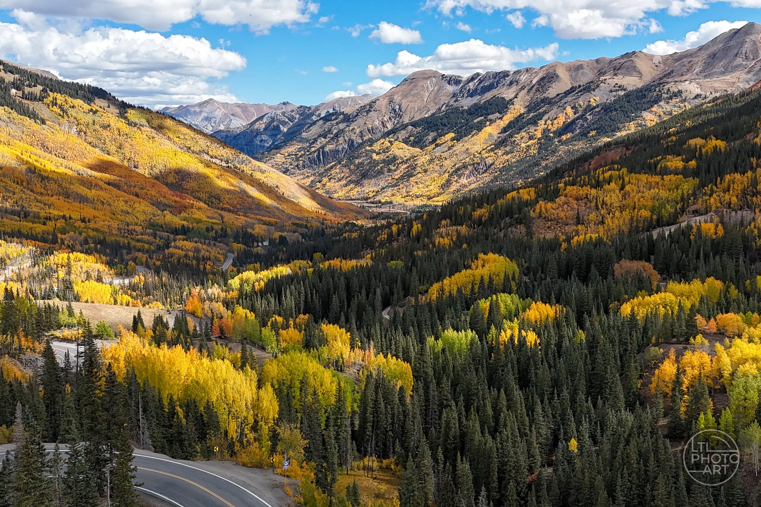Golden aspens, evergreen forest, mountain ridges, and the winding Million Dollar Highway above Red Mountain Creek near Silverton, Colorado.