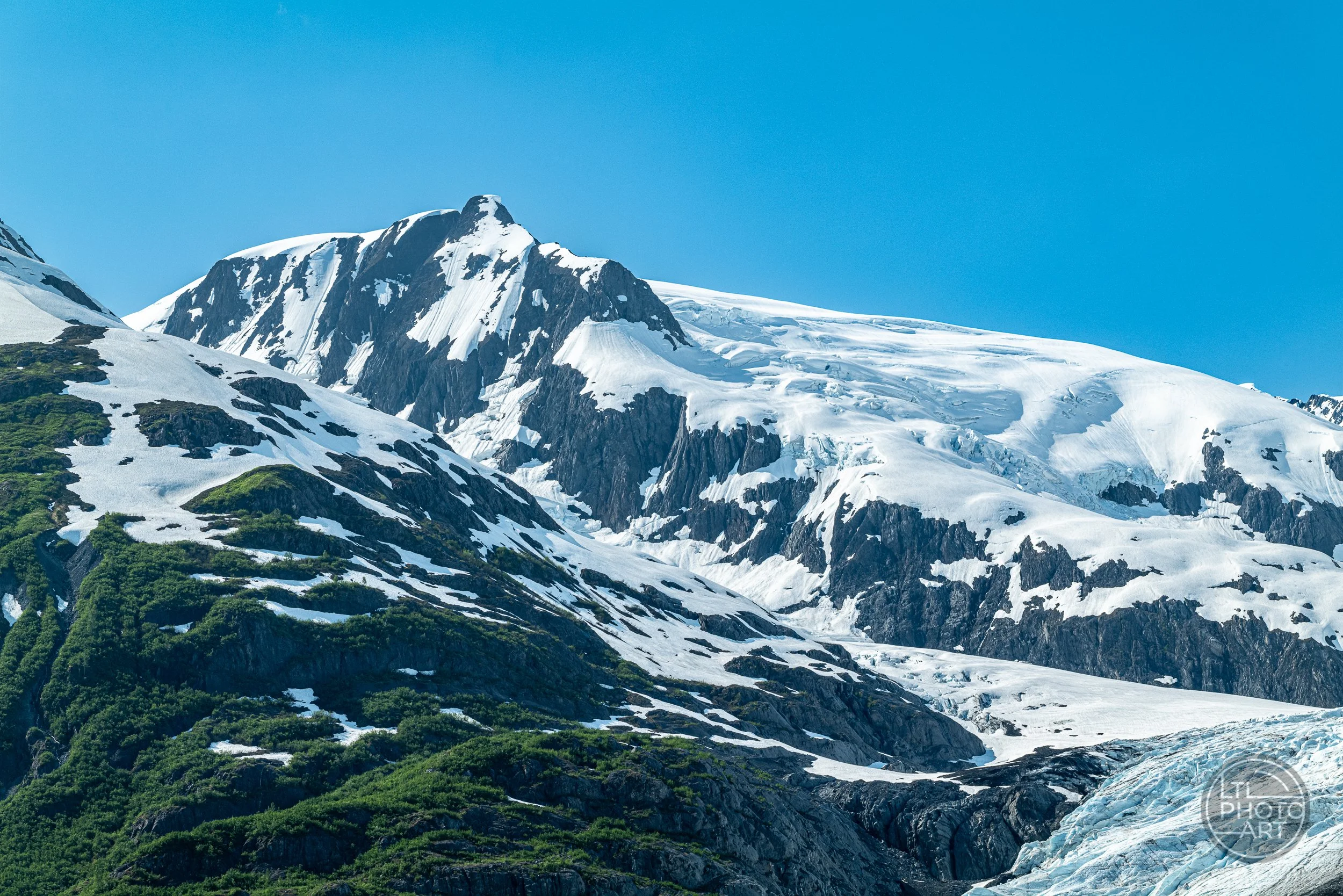 Snow-covered peaks, exposed dark rock, and glacial ice in the Chugach Mountains near Whittier, Alaska.