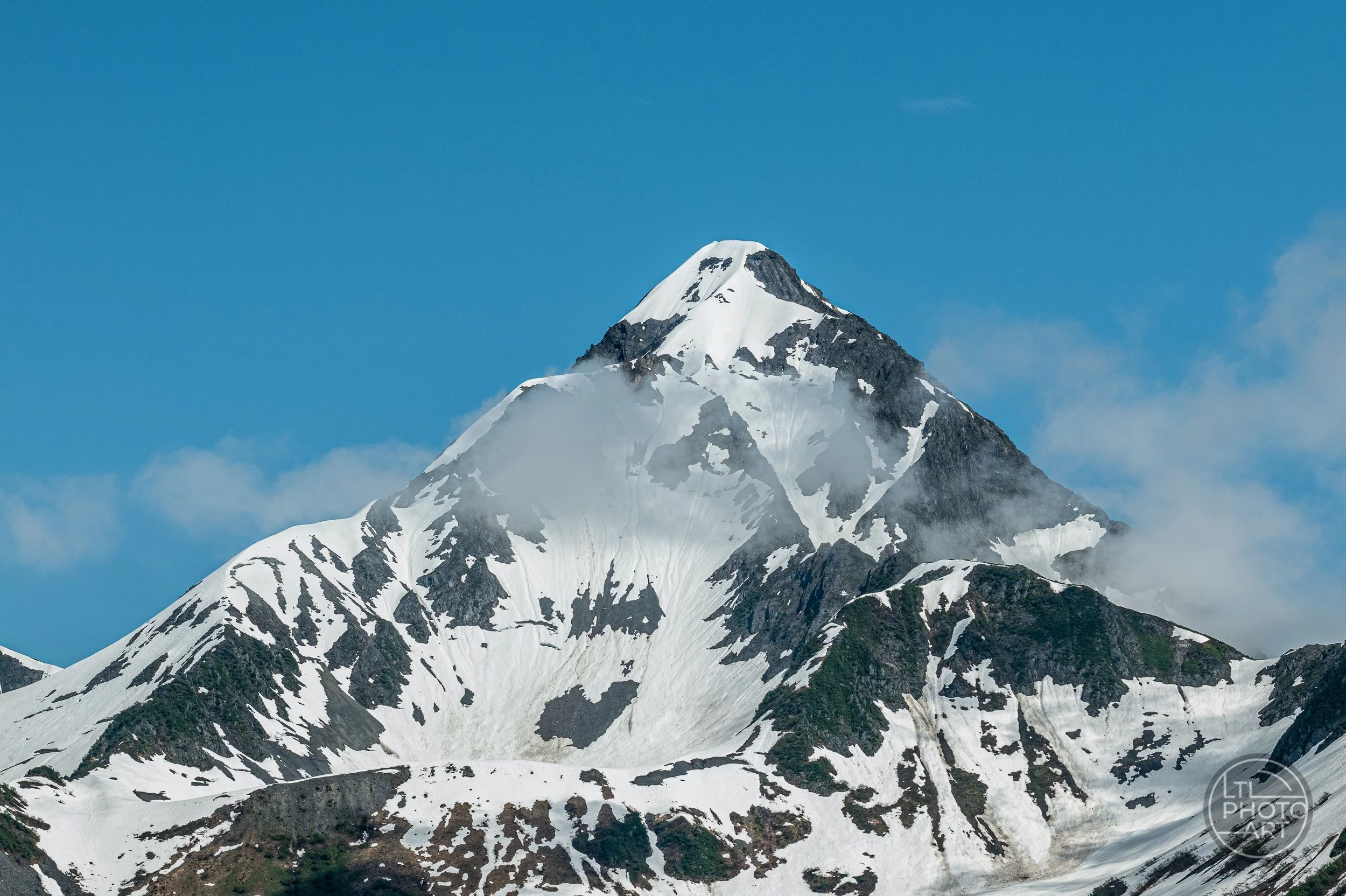 Snow-covered mountain peak surrounded by clouds in the Kenai Mountains of Kenai Fjords National Park, Alaska.