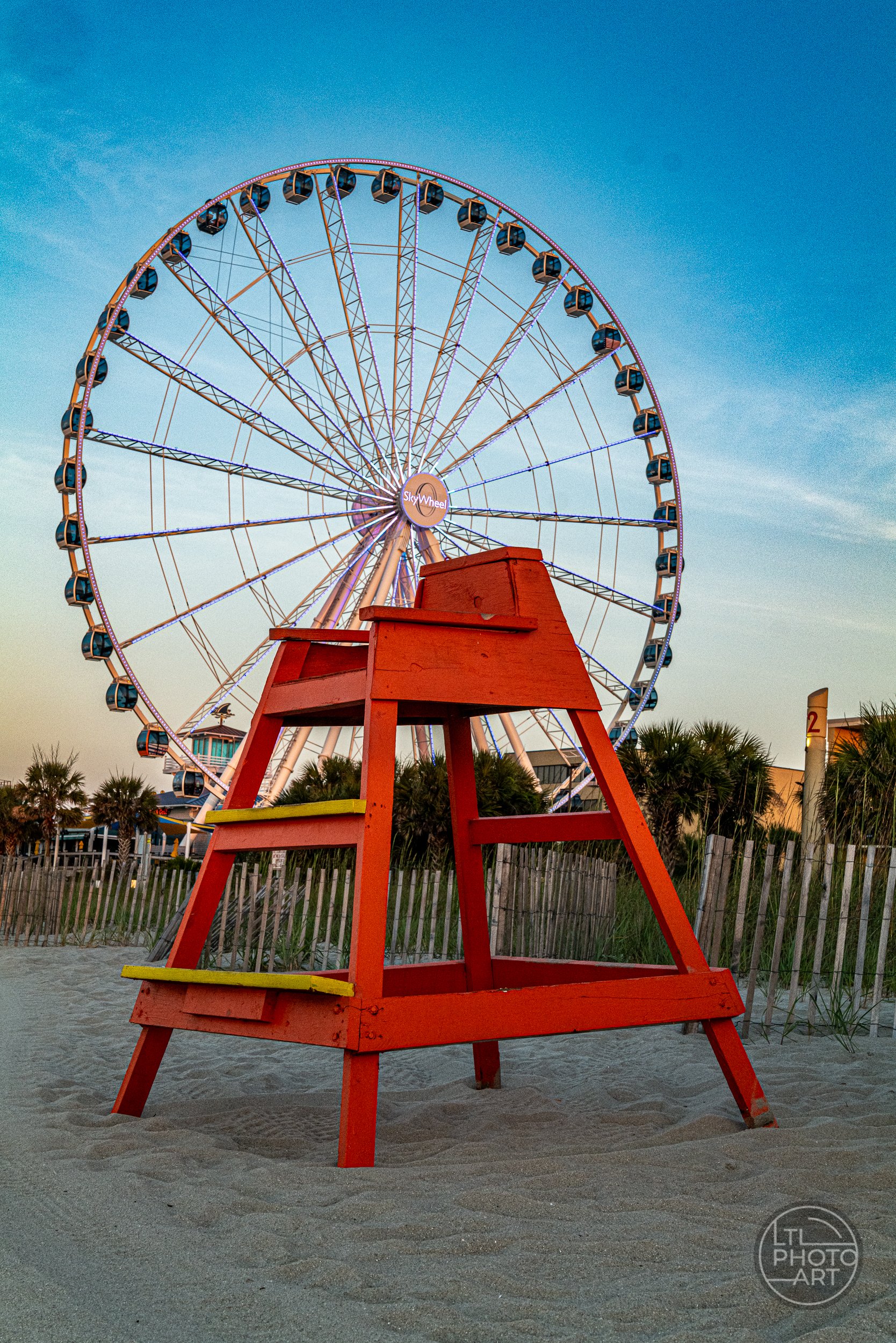 Red lifeguard chair on Myrtle Beach, South Carolina, with the SkyWheel in the background near the Myrtle Beach Boardwalk and Plyler Park.