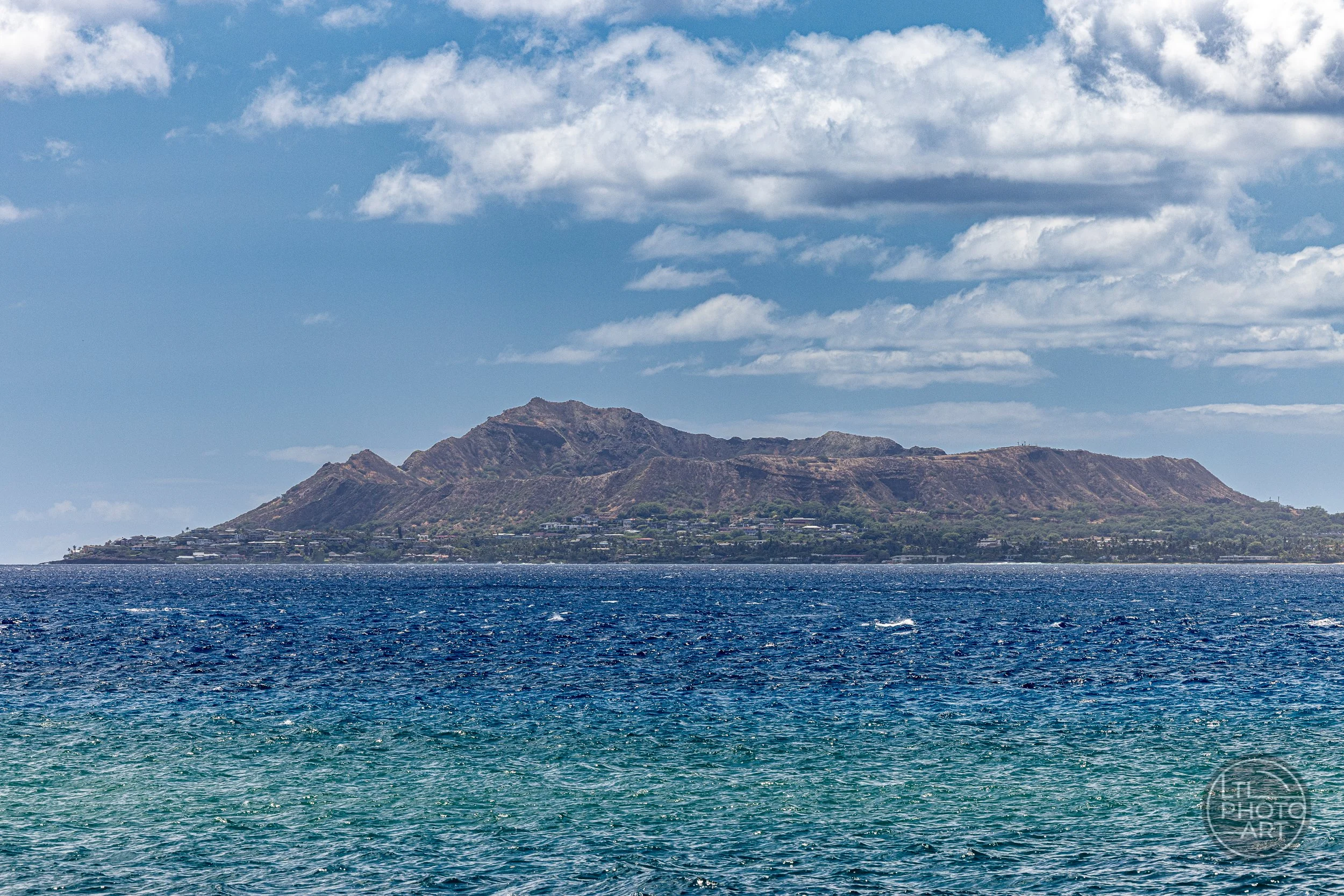 Diamond Head crater on Oahu, Hawaii, viewed from the Pacific Ocean, with deep blue water in the foreground and scattered clouds overhead.