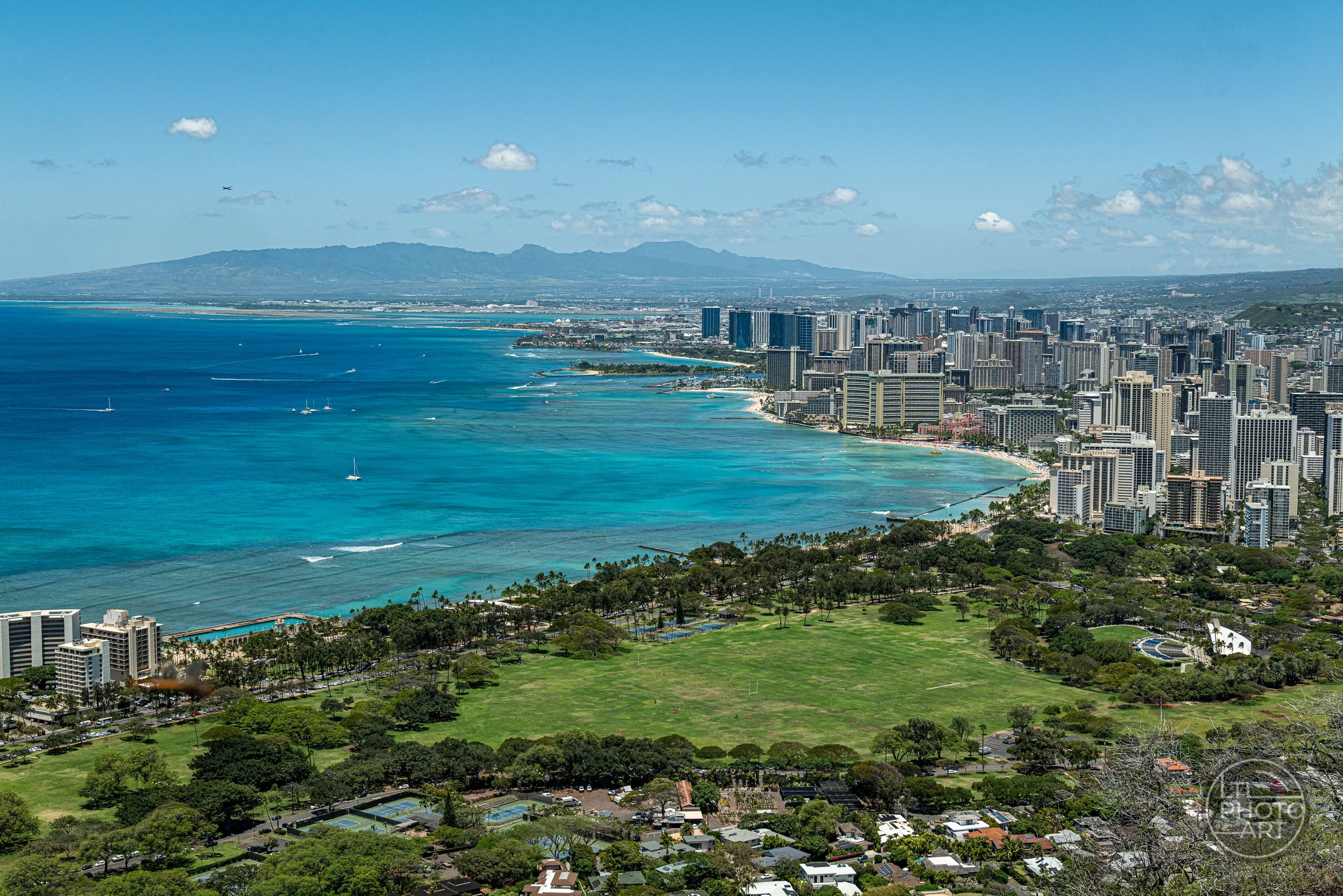 Panoramic view of Waikiki and Honolulu from the summit of Diamond Head on Oahu, with turquoise Pacific waters, beaches, city buildings, and green parkland below.