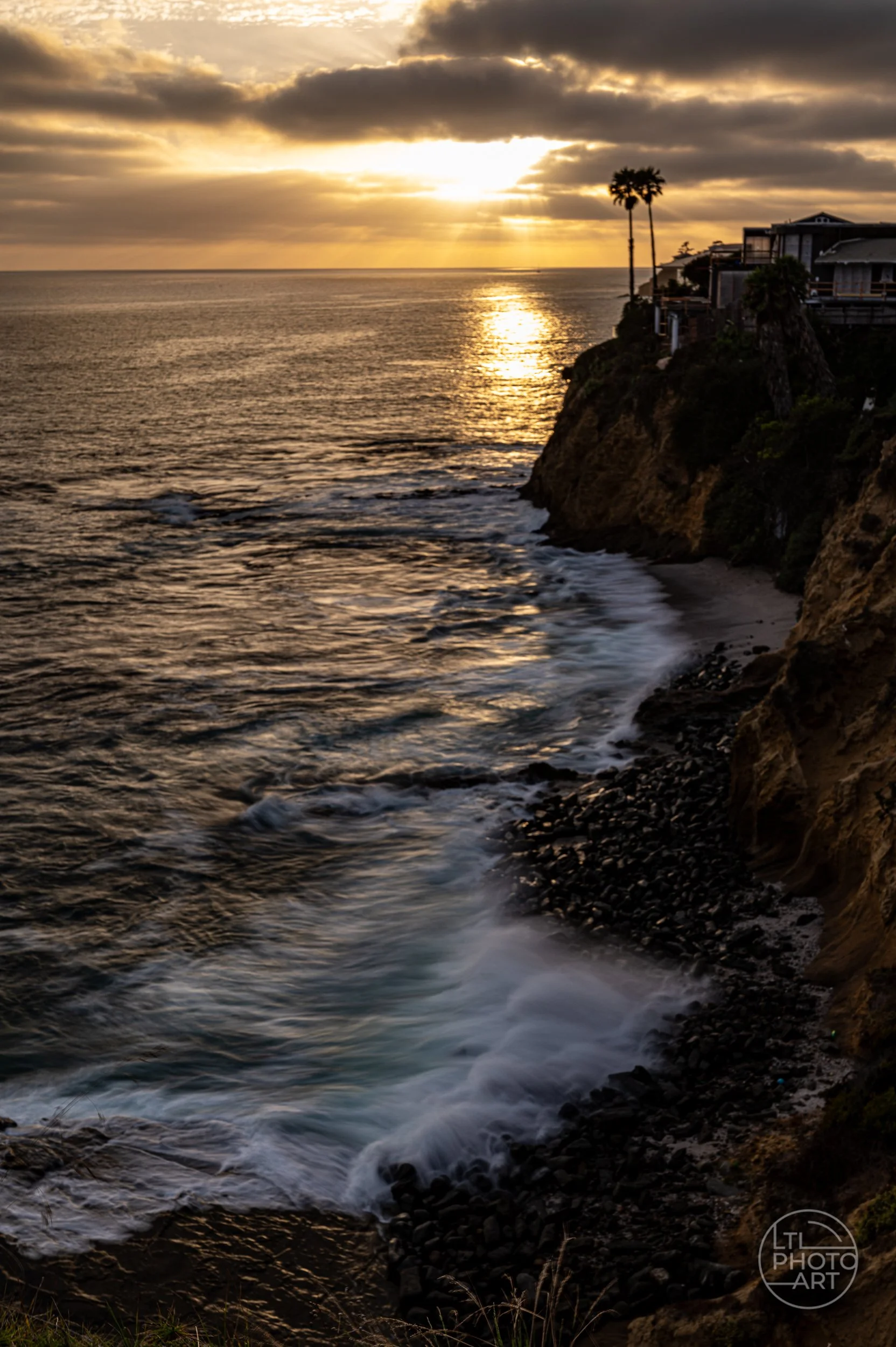 Golden sunset over the Pacific with waves moving along a rocky cove below Crescent Bay Point Park in Laguna Beach.
